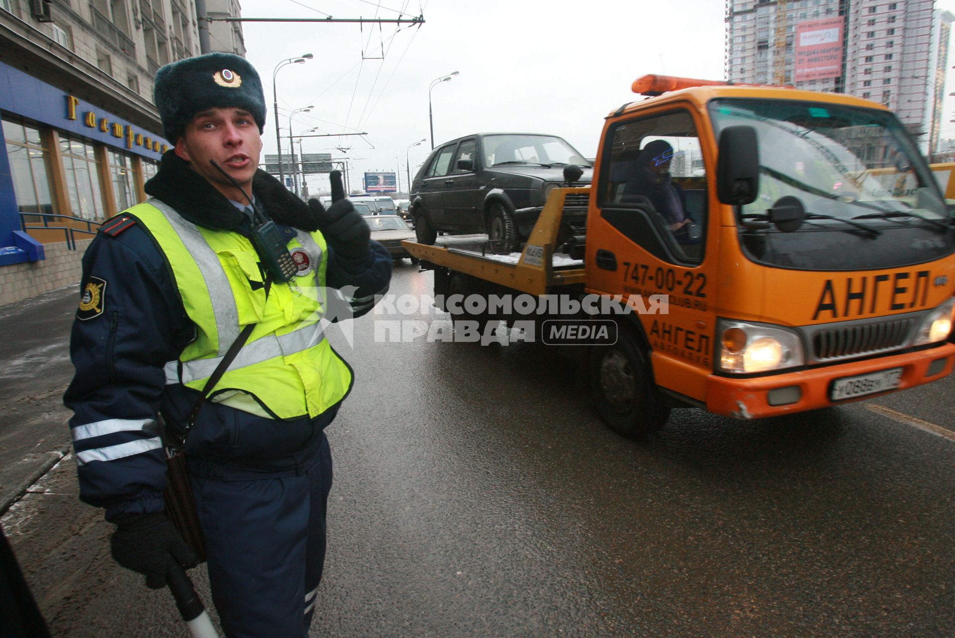 Сотрудник ДПС несет службу на оживленной улице, мимо проезжает автомобиль эвакуатор на борту везущий другой автомобиль ГОЛЬФ. 13 декабря 2007 года.