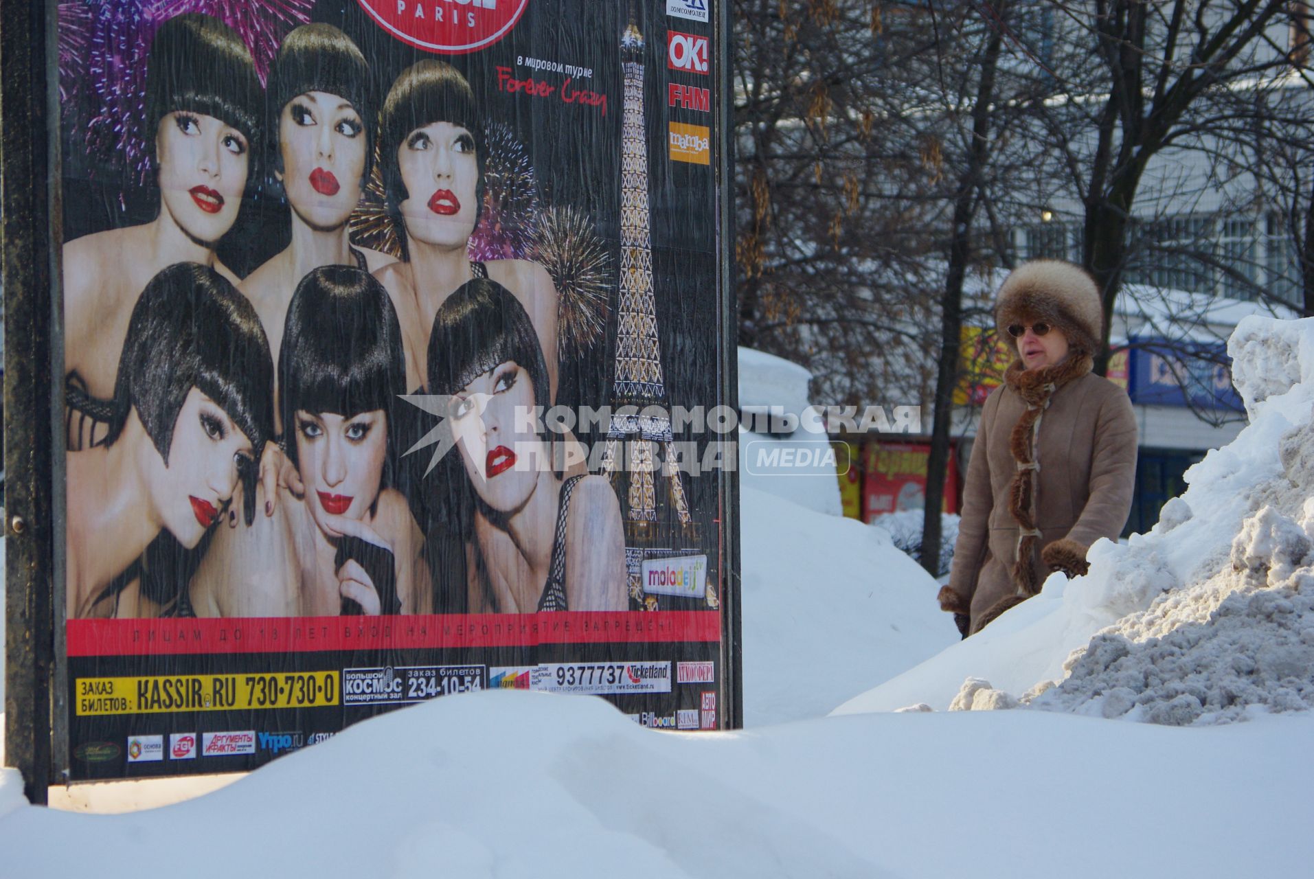 Москвичка проходит мимо рекламного плаката, 16 февраля 2011 года. Снег. Зима. Холод. Мороз. Уборка снега. Сугроб. Коммунальное хозяйство. Гололед. Реклама уличная.