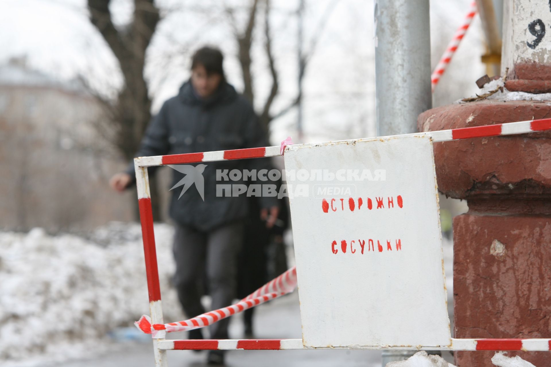 На углу дома стоит табличка с надписью- ОСТОРОЖНО СОСУЛЬКИ мимо проходит мужчина. 3 марта 2011 года.