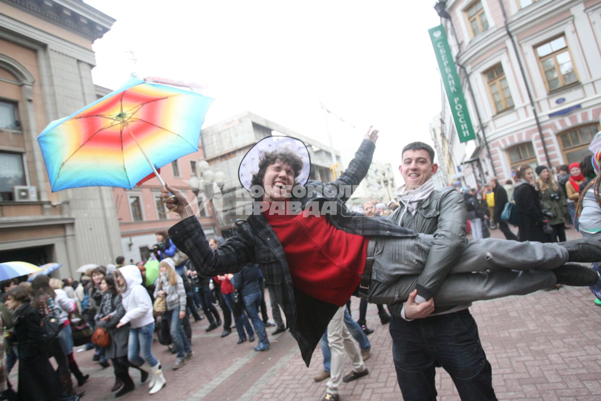 Парень размахивает зонтом,  лежа на руках у друга, Москва, 10 апреля 2011 года