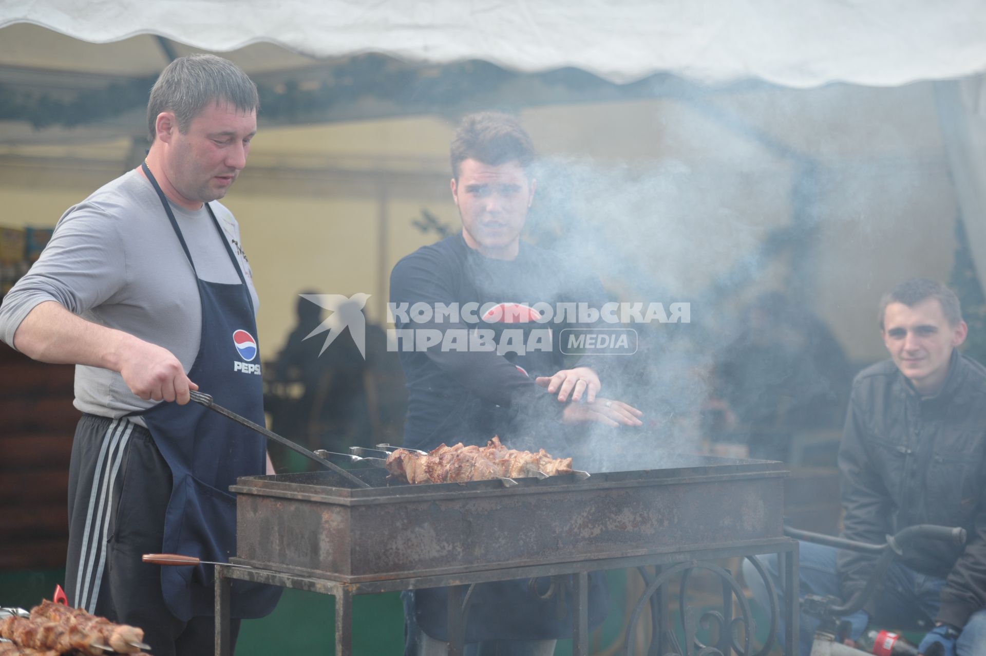 Над мангалом с шашлыком молодой человек греет руки, отдых в парке ВДНХ, Москва, 5 мая 2011 года