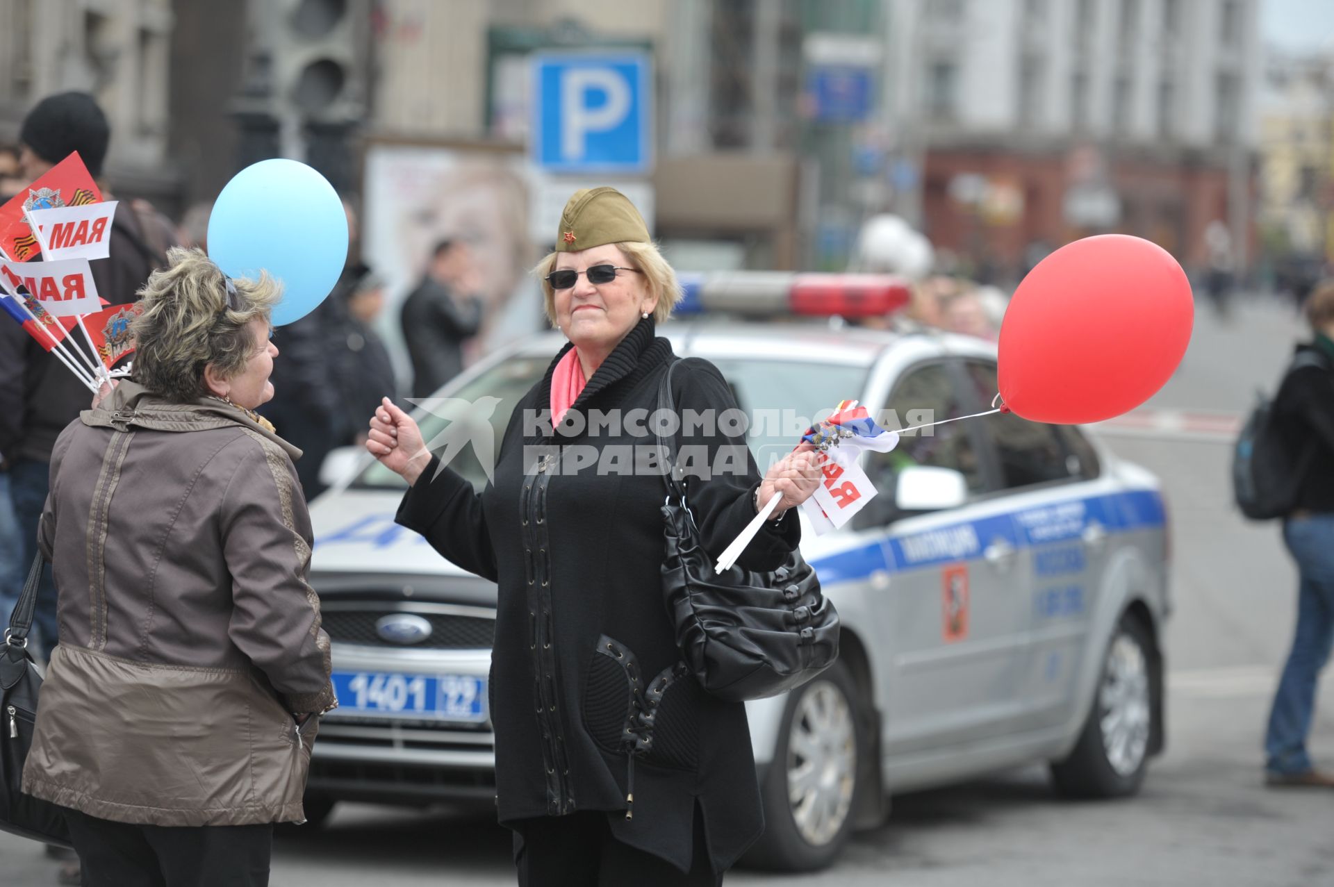 Женщина в военной пилотке с флажками в руках танцует на улице города, Москва, 1 мая 2011 года