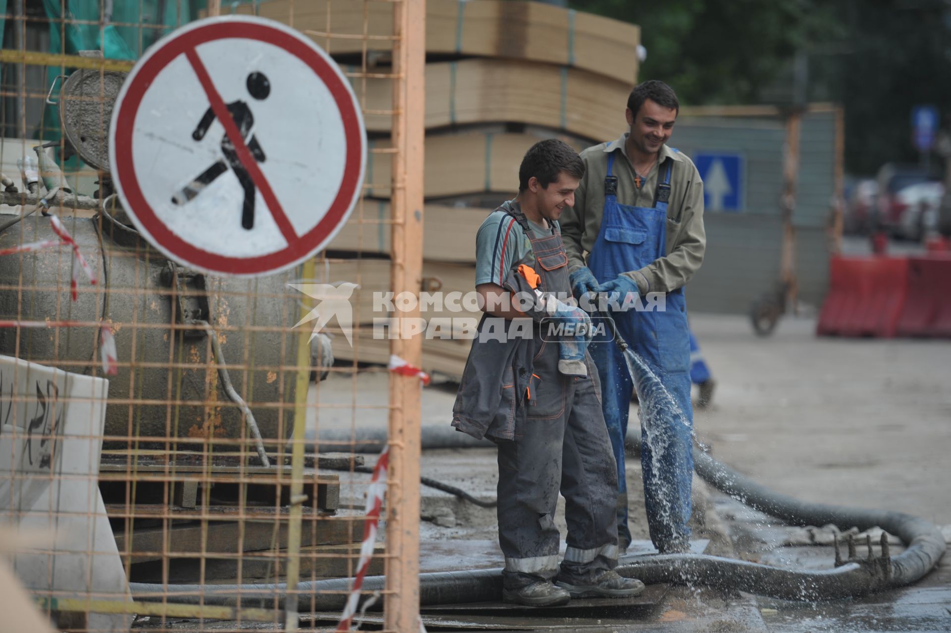 Гастарбайтеры из шланга поливают асфальт на стройке, Москва, 28 июня 2011 года