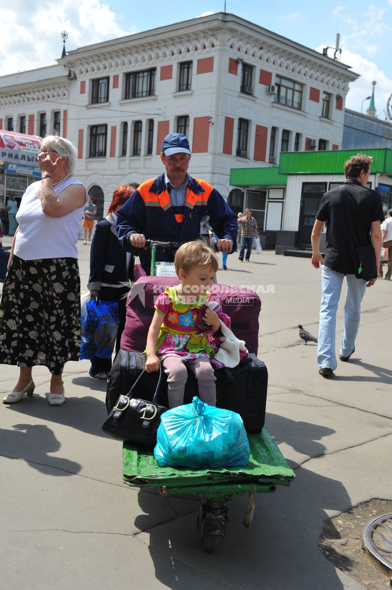 Пассажиры на железнодорожном  ярославском вокзале в Москве летом. Перевозка багажа. Мужчина везет ребенка на тележке. 31 мая 2011 г.