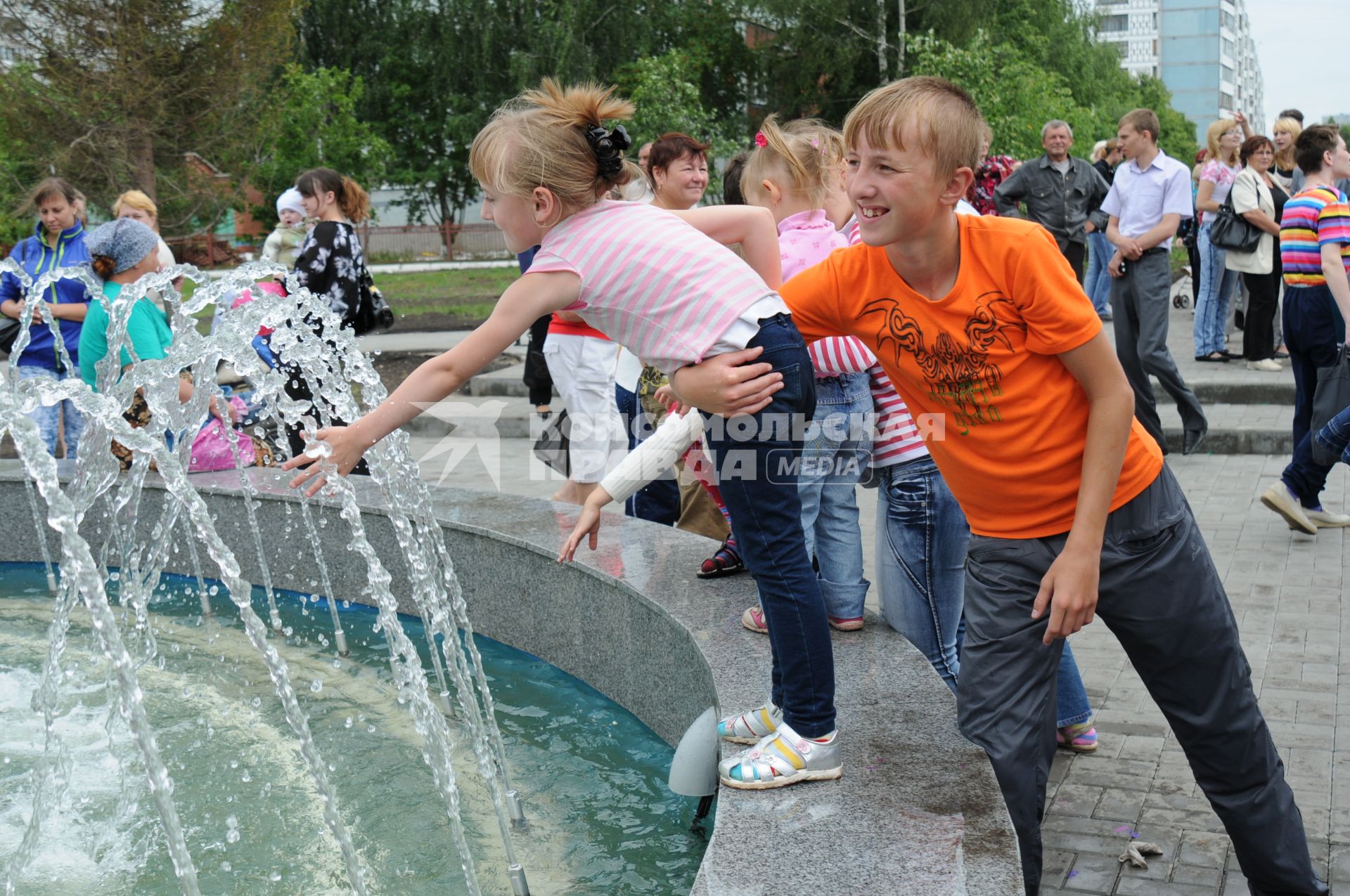 Брат придерживая рукой сестру не дает ей упасть в фонтан. Сестра моет руки в фонтане. 6 июля 2011 года.  Новосибирск.