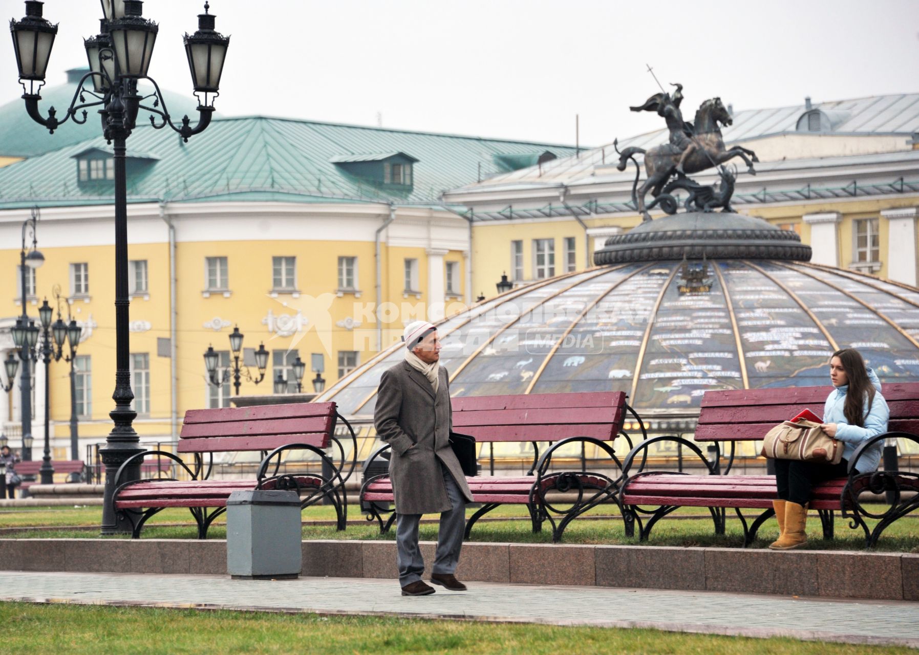 Москва центр города, люди. Мужчина идет по Манежной площади мимо молодой девушки, которая сидит на скамейке. 15 Декабря 2011 года