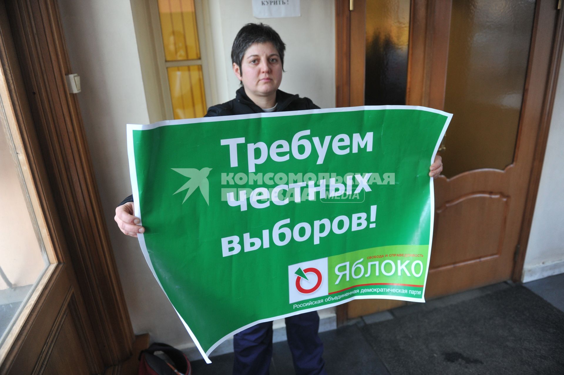 Женщина держит плакат пратии ЯБЛОКО с надписью ТРЕБУЕМ ЧЕСТНЫХ ВЫБОРОВ!. 27 января 2012 года.