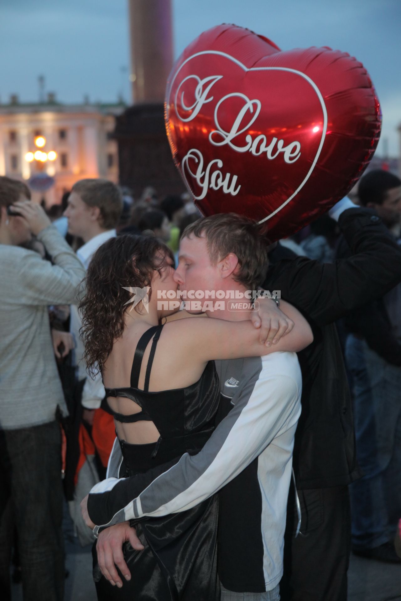 Молодая пара стоит на улице и целуется. В руках у девушки воздушный шарик с надписью `I love you`.