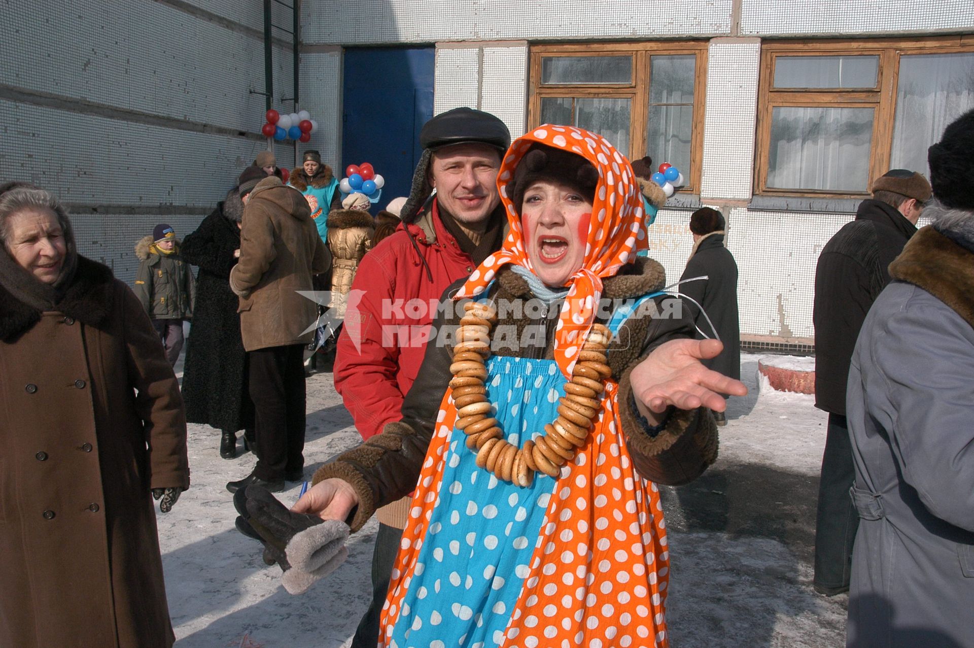 Женщина в праздничном наряде масленицы со связкой баранок на шее зазывает людей.