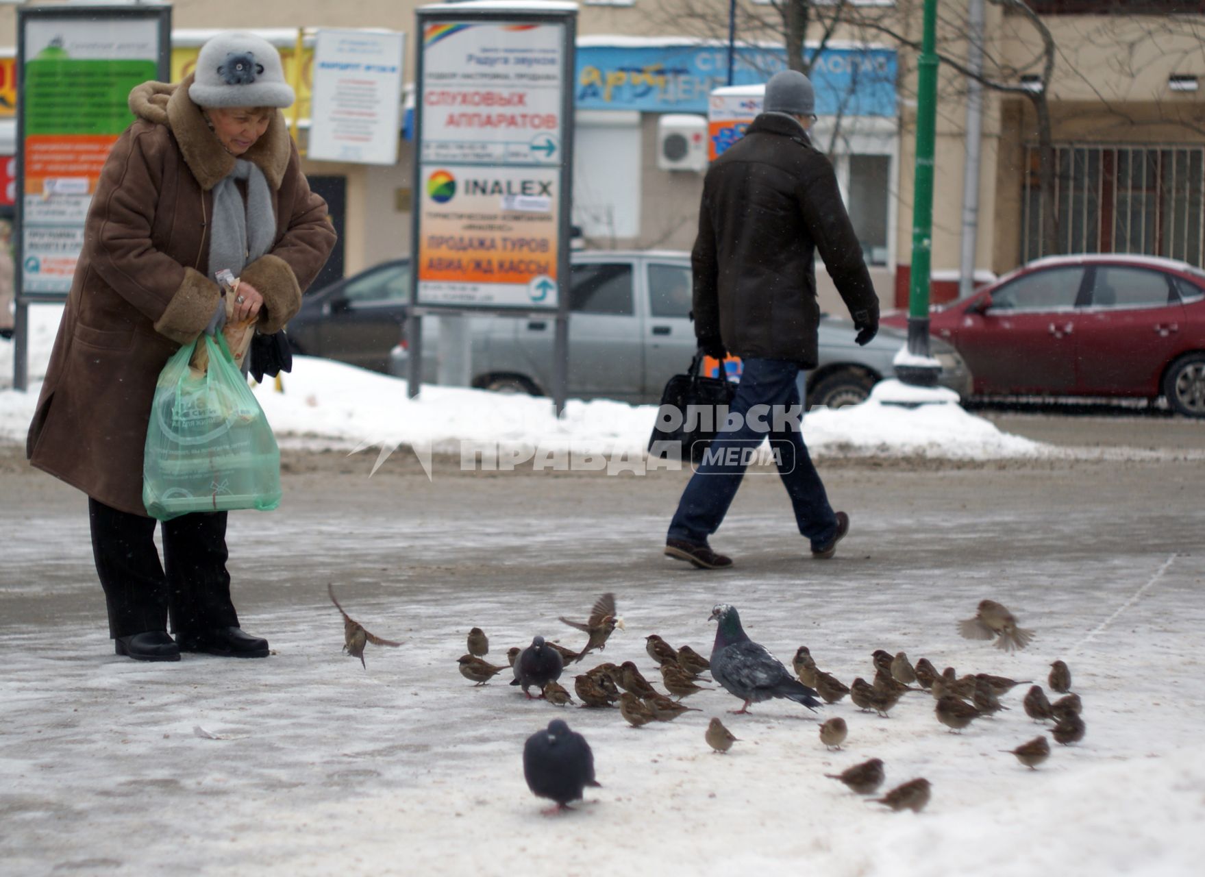 Женщина стоит посреди улицы и кормит птиц.
