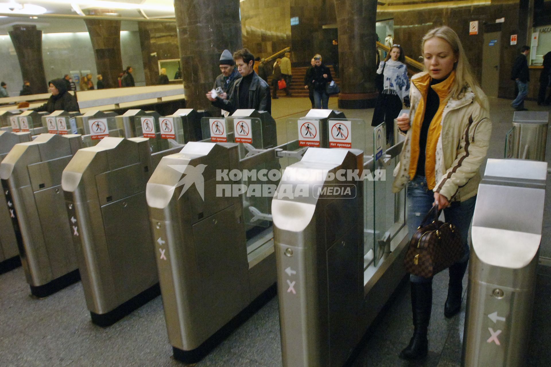 Люди проходят через турникеты в метро.