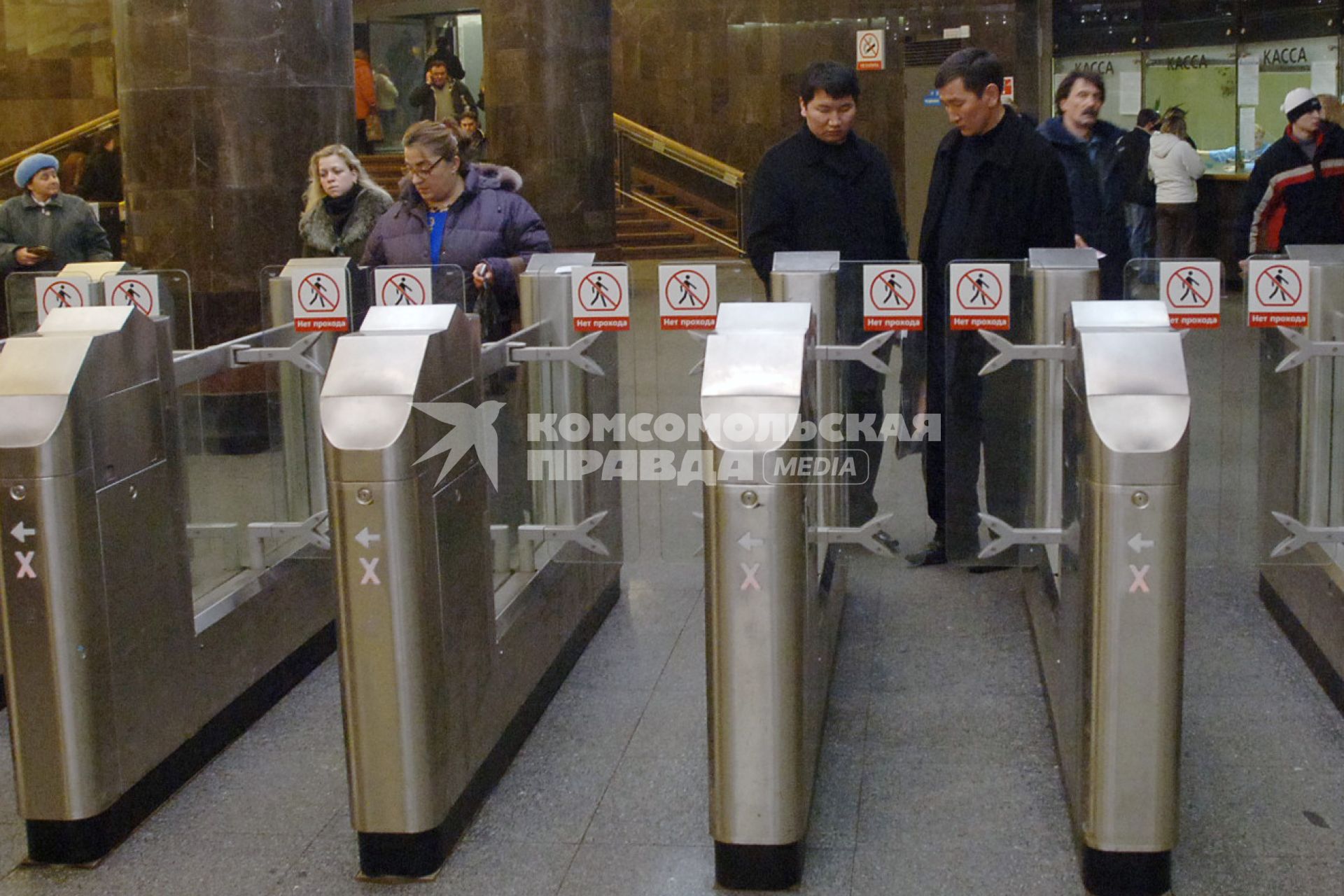 Люди стоят перед турникетами в метро. Двое молодых людей азиатской внешности.