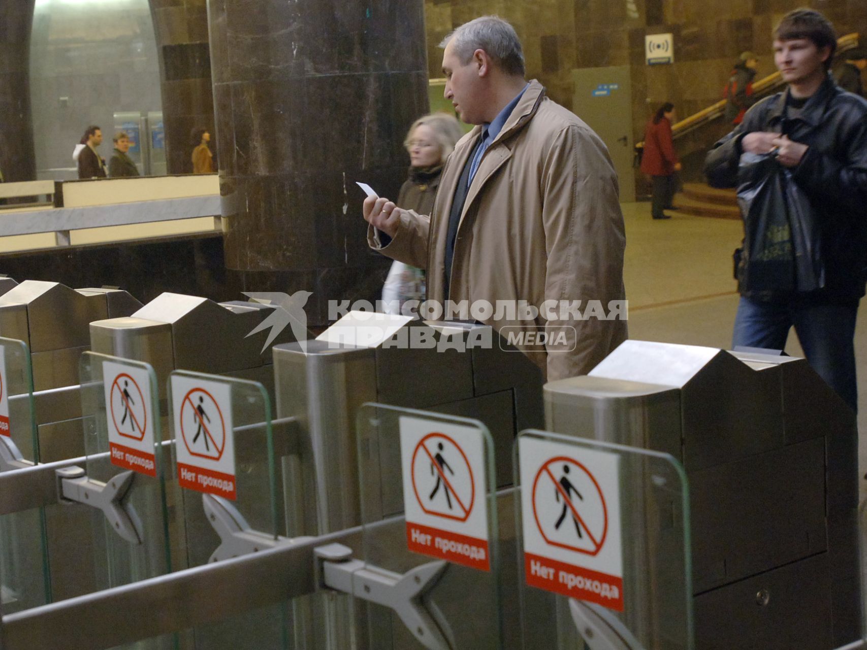 Мужчина стоит перед турникетом на вход в метро, рассматривает проездной билет который держит в руках.