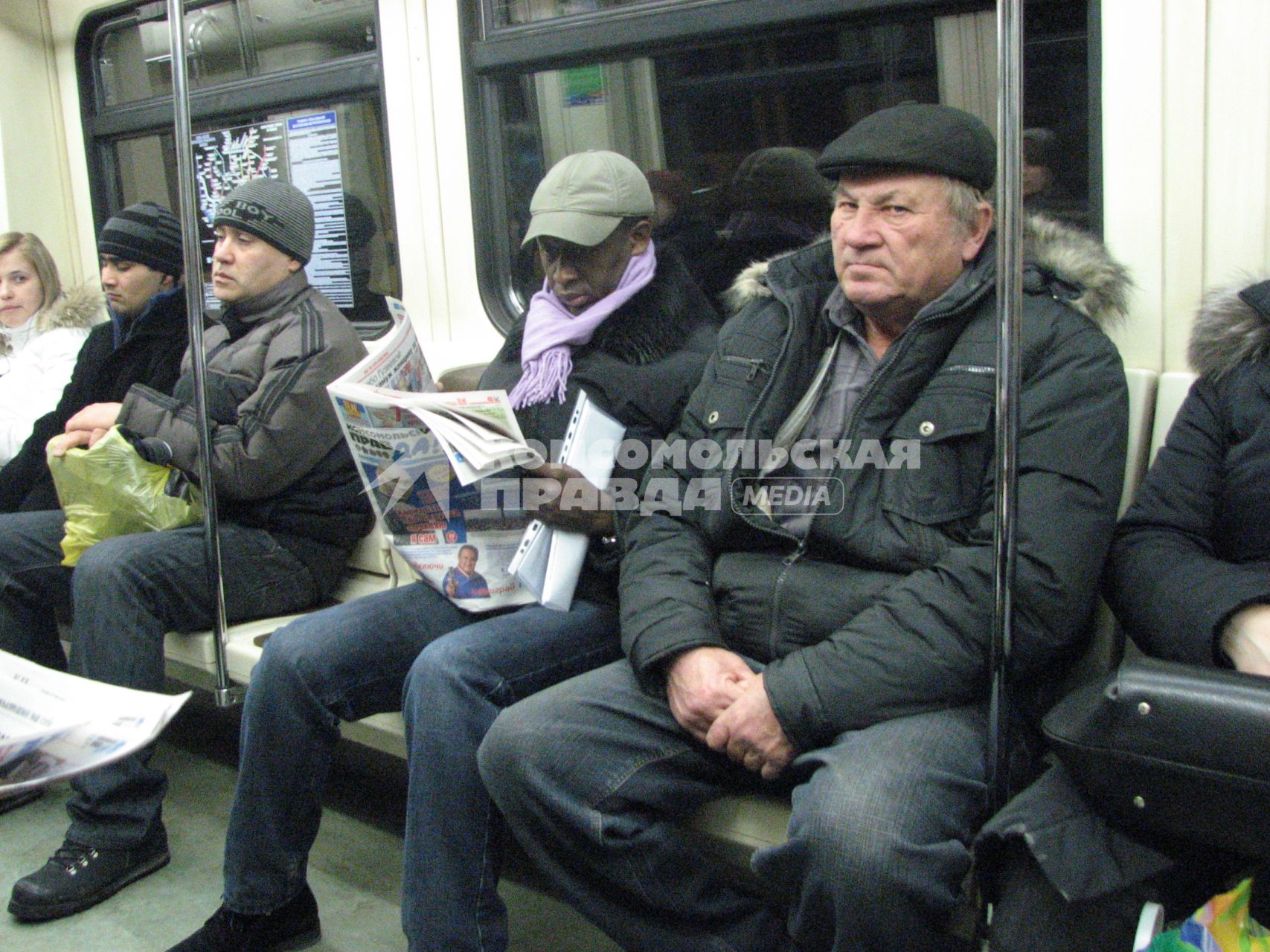 Человек негроидной расы читает газету Комсомольская правда едя в метро.