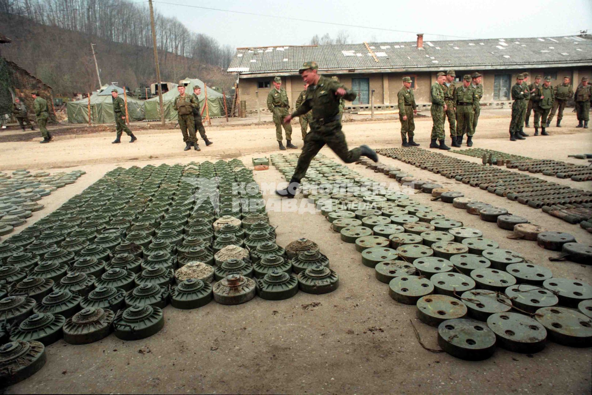 На плацу военного лагеря разложены мины.
Солдат перепрыгивает через ряды мин.