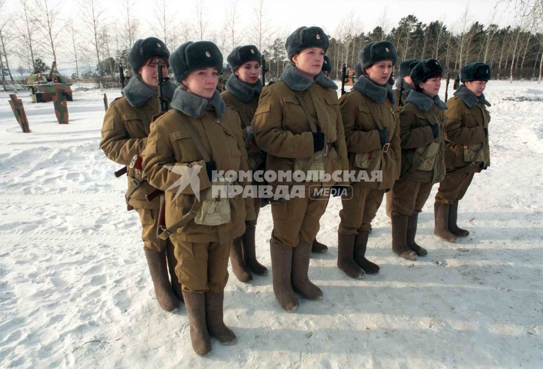 Девушки в военной форме с автоматами за спиной выстроились на площадке  для военный учений.