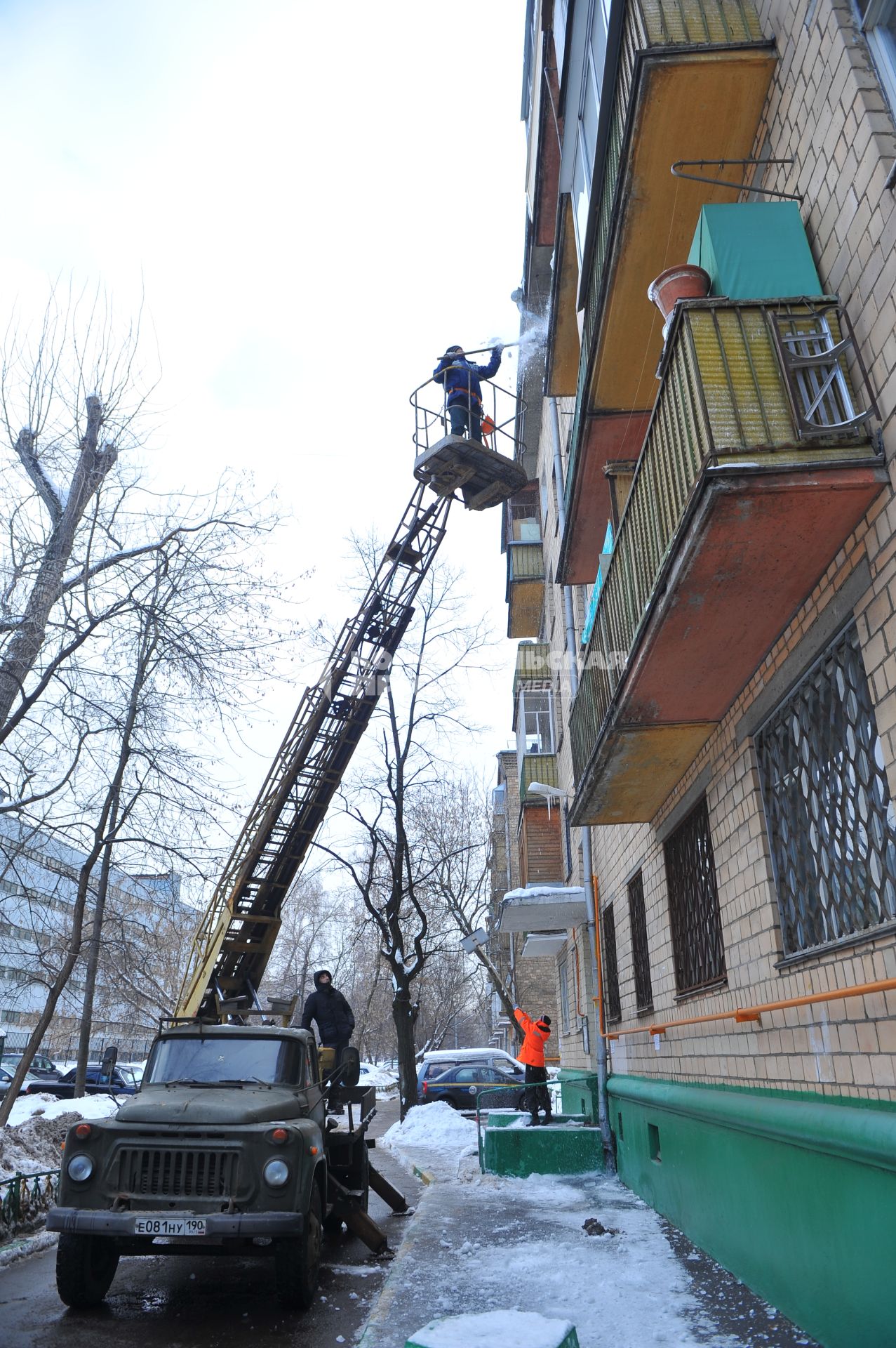 Очистка балконов от снега и наледи. На снимке: рабочий сбрасывает снег с балкона.