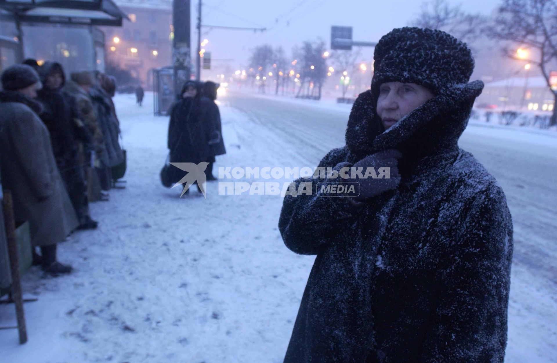 Люди на остановке во время метели в городе.