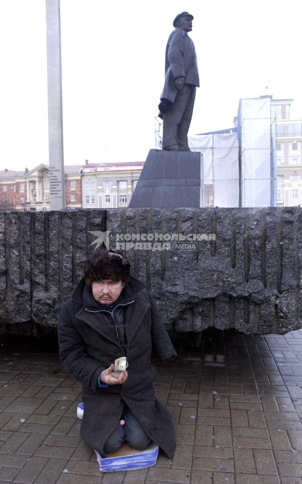 Нищий сидит около памятника Ленину и просит подаяние.