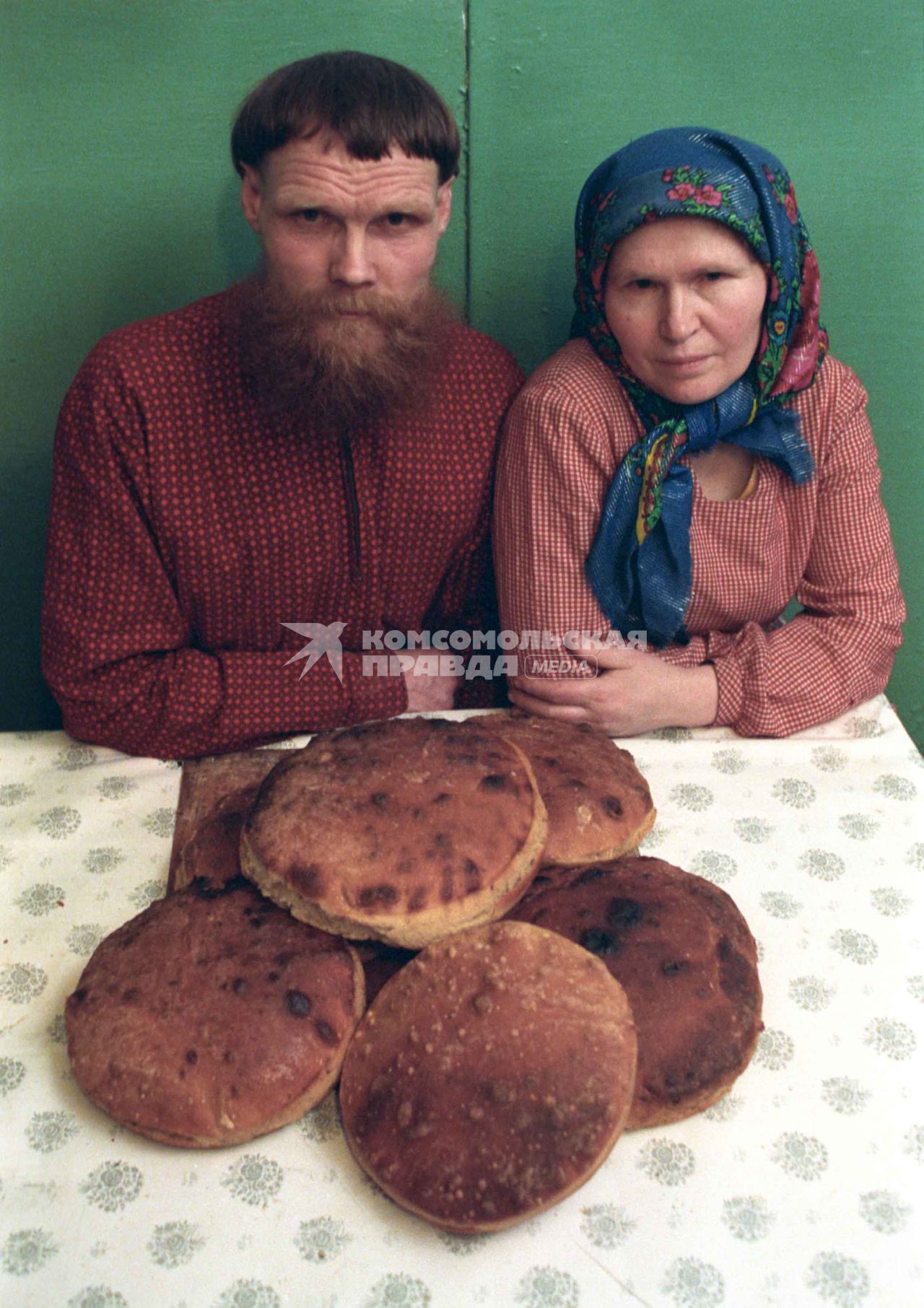 Двое сидят за столом, на котором лежит свежеиспеченный хлеб.