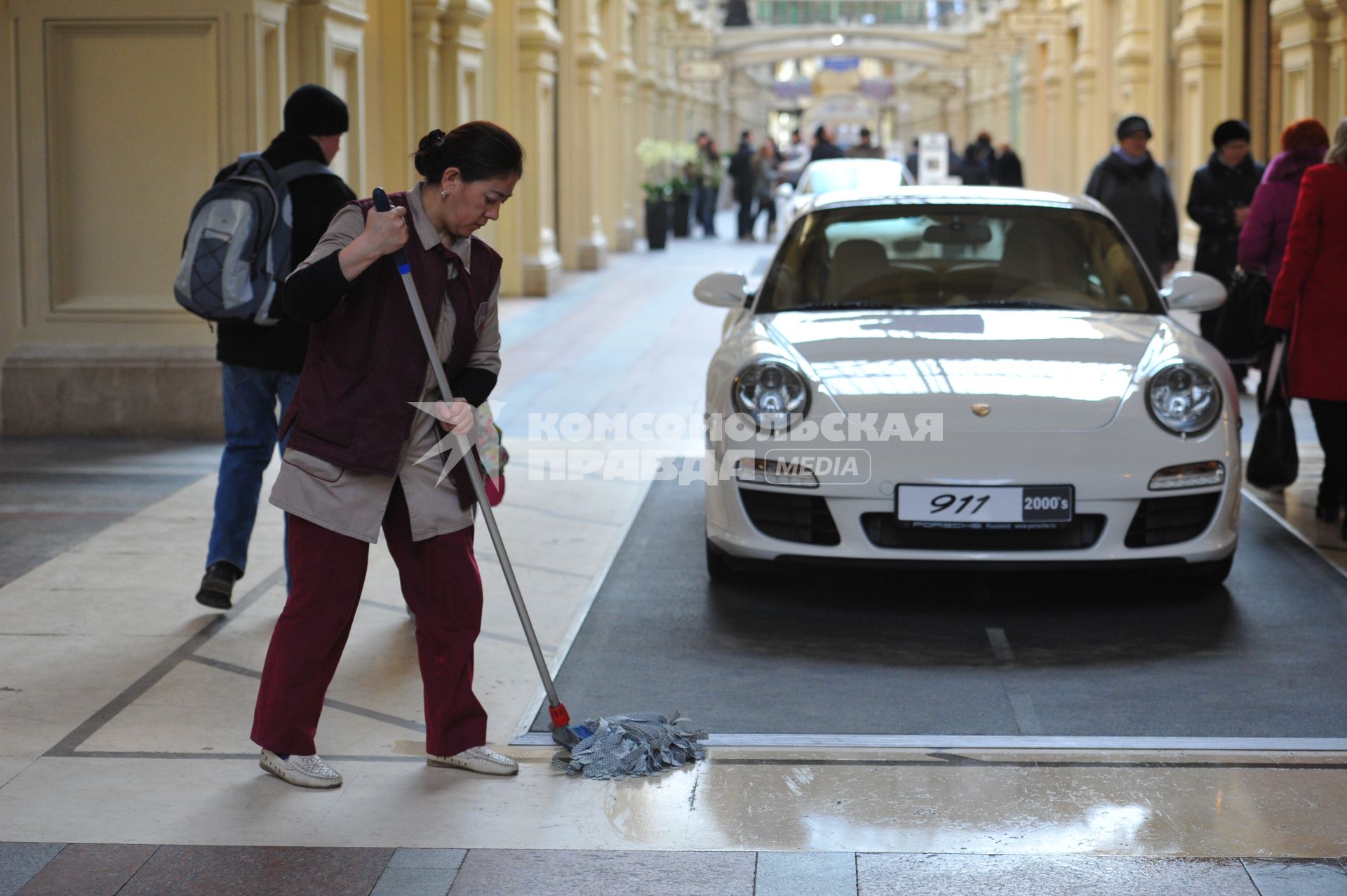 ГУМ. Выставка уникальных автомобилей Porsche, расположенных вдоль первой линии магазина, которая была временно стилизована под `Улицу Porsche`.На снимке: уборщица и автомобиль Porsche.