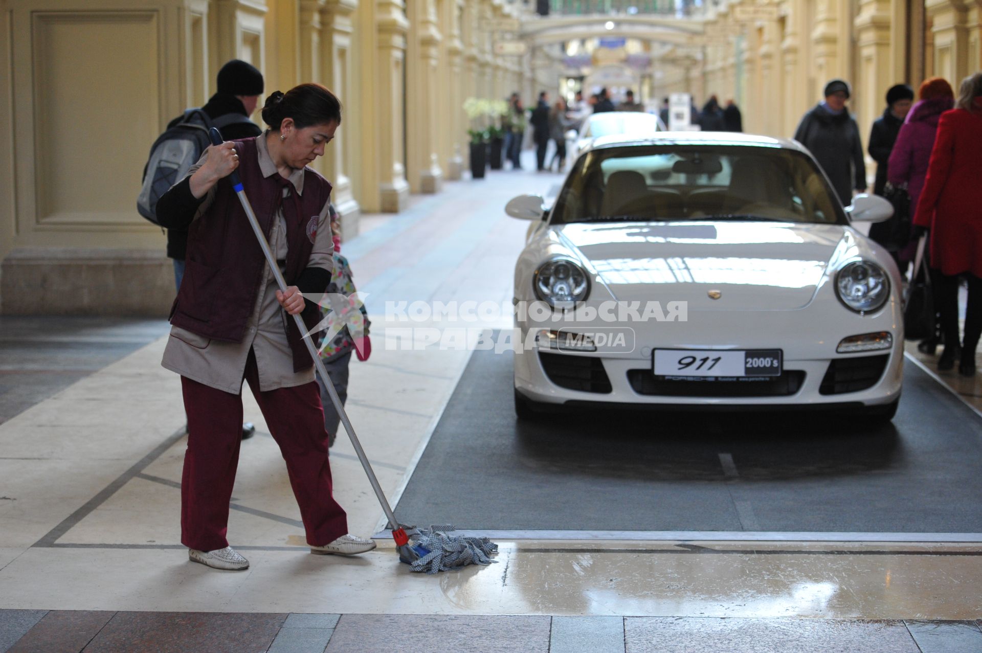 ГУМ. Выставка уникальных автомобилей Porsche, расположенных вдоль первой линии магазина, которая была временно стилизована под `Улицу Porsche`.На снимке: уборщица и автомобиль Porsche.