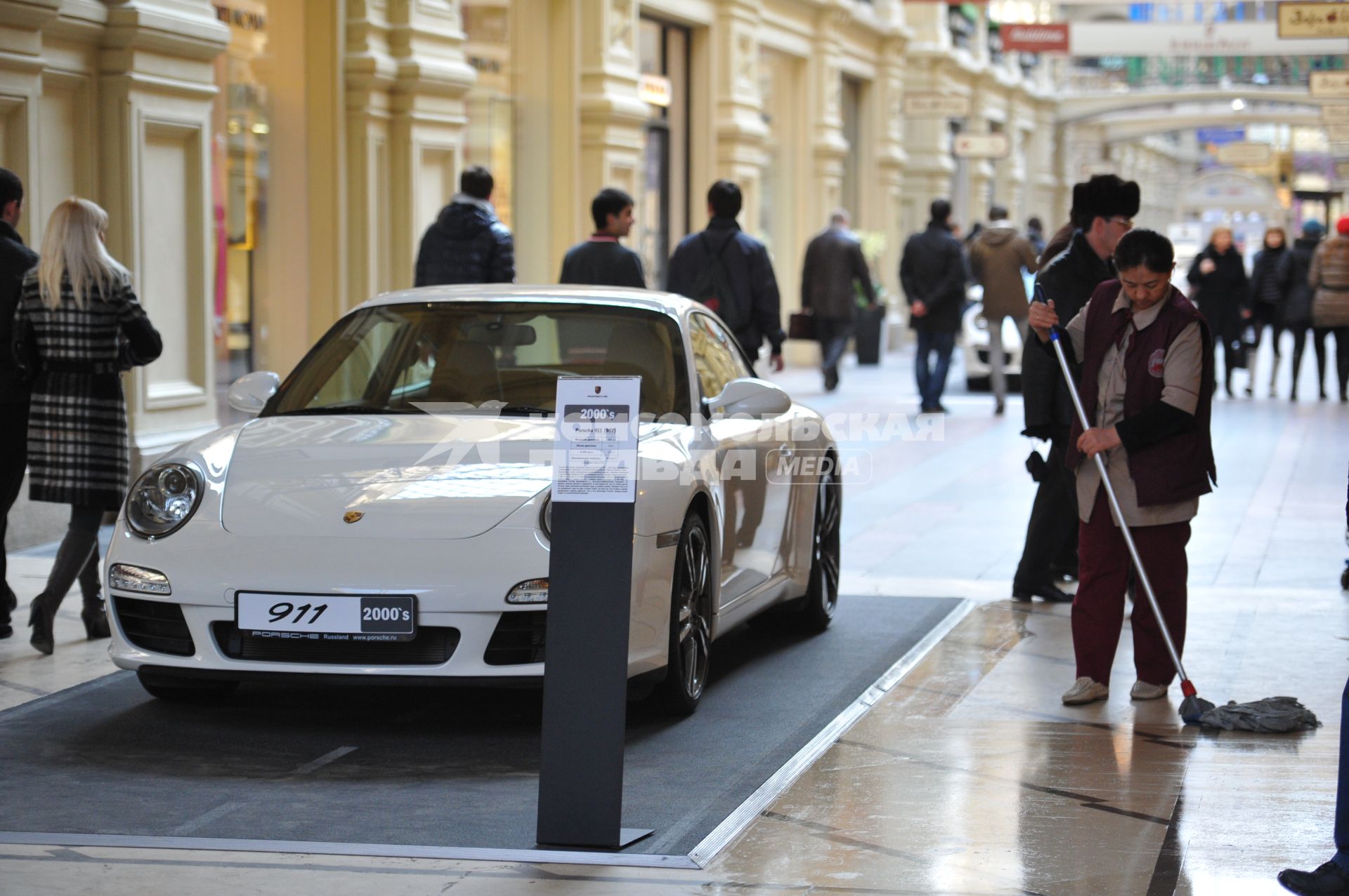 ГУМ. Выставка уникальных автомобилей Porsche, расположенных вдоль первой линии магазина, которая была временно стилизована под `Улицу Porsche`.На снимке: уборщица и автомобиль Porsche.