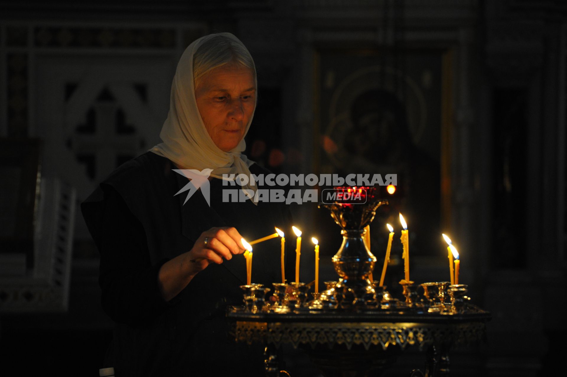 Женщина поджигает свечу в храме.