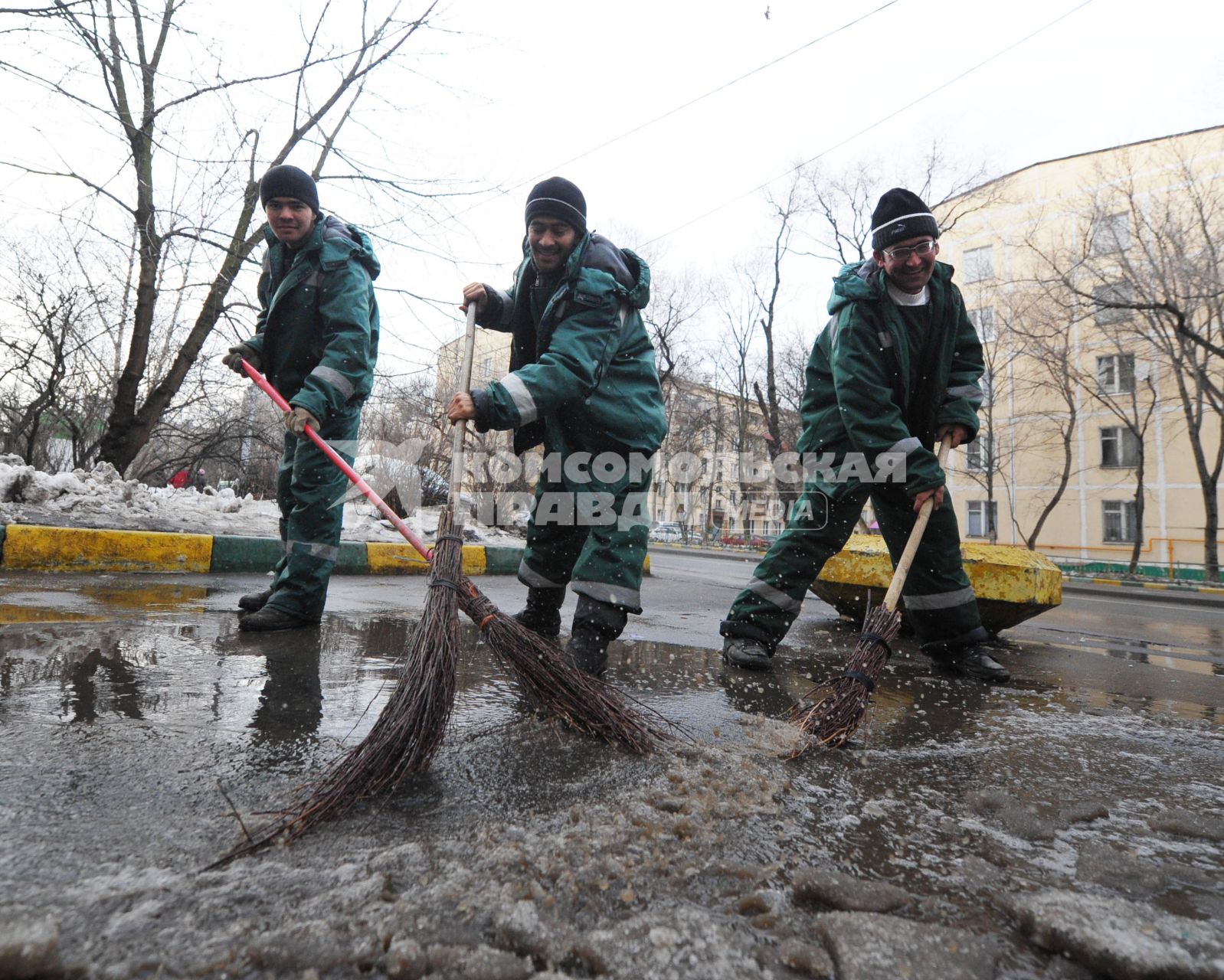 Гастарбайтеры метлой сметают лужу с дороги.