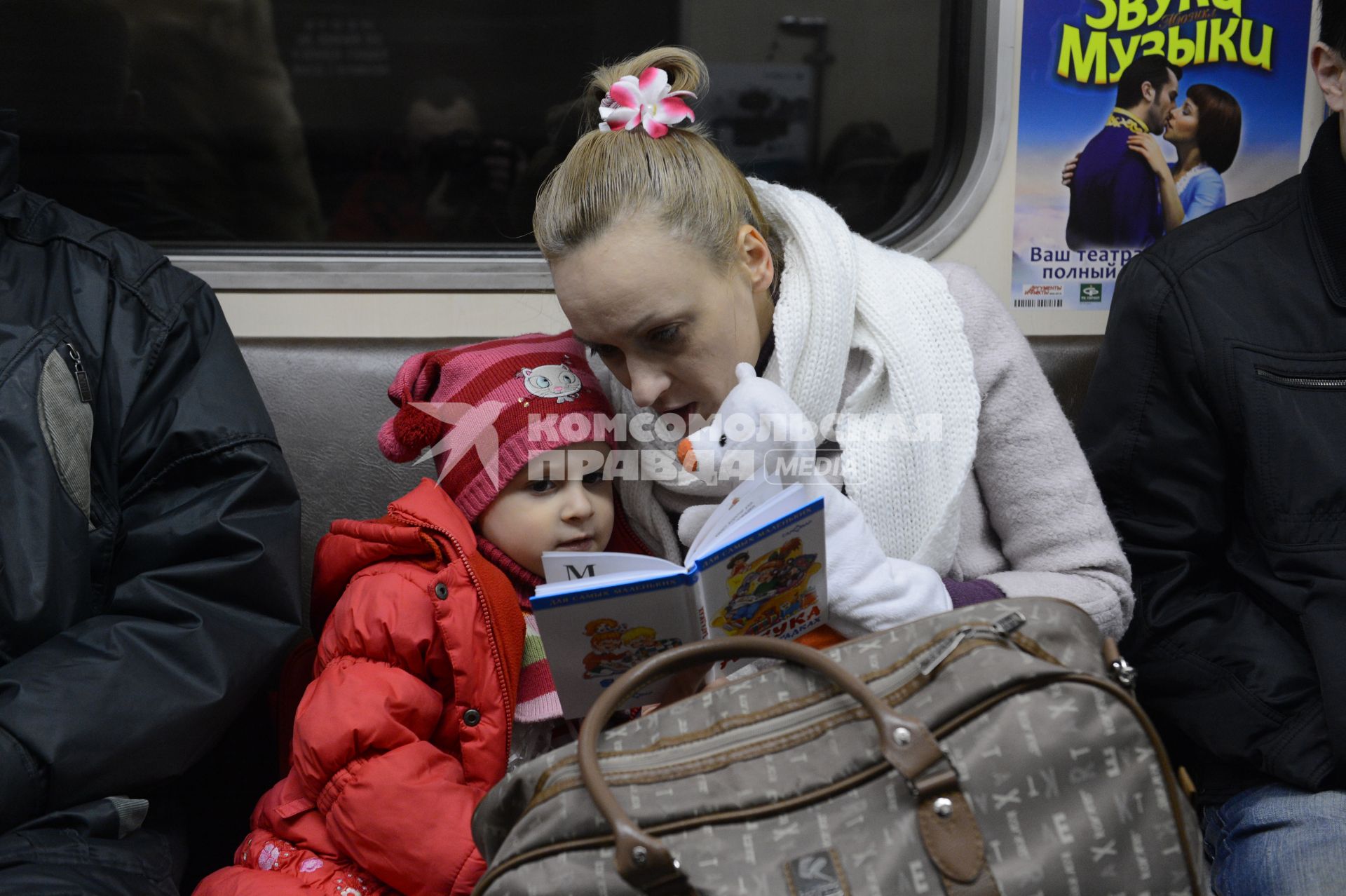 Мать дочери  читает книгу во время поездки в метро.