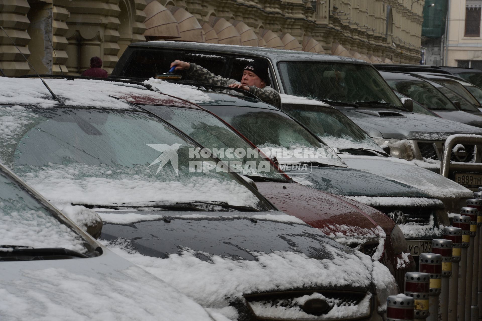 Мегаполис. Автомобильная парковка. На снимке: мужчина счищает снег с автомобиля.