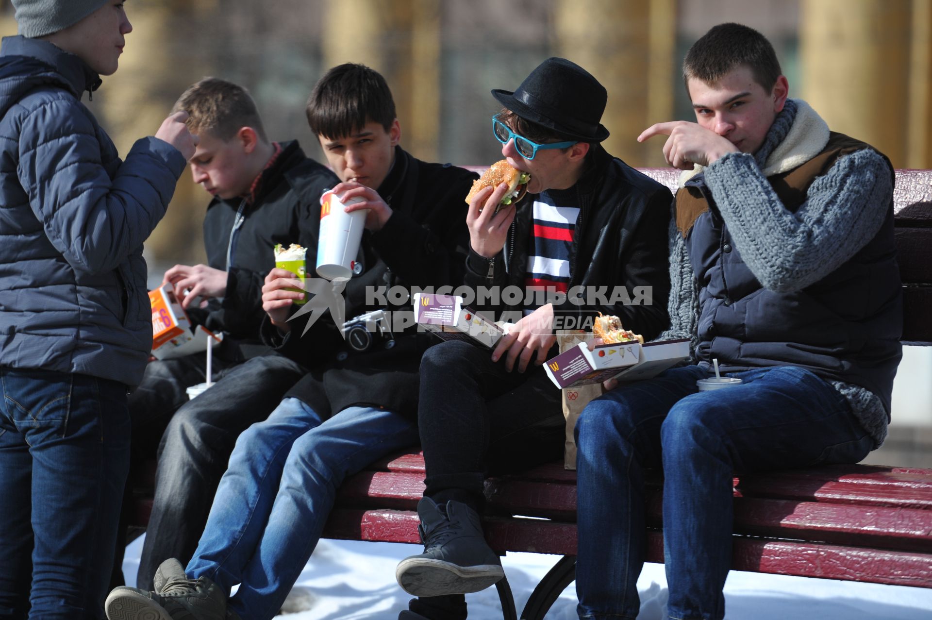 Молодые люди едят фаст-фуд на улице.