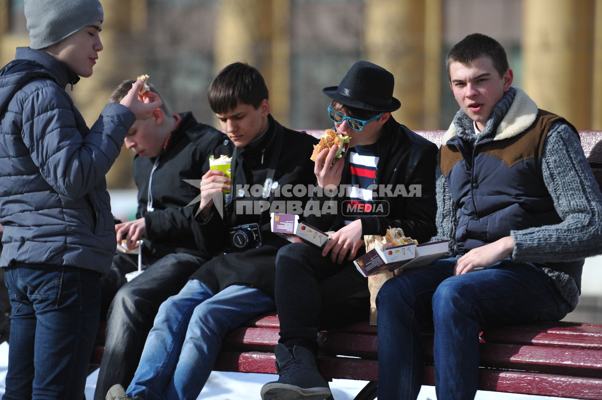 Молодые люди едят фаст-фуд на улице.