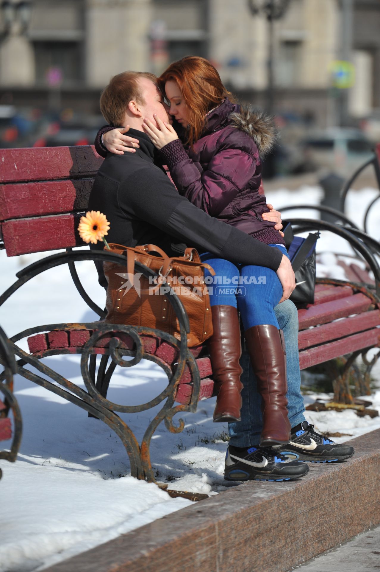 Молодая пара целуется на скамейке.