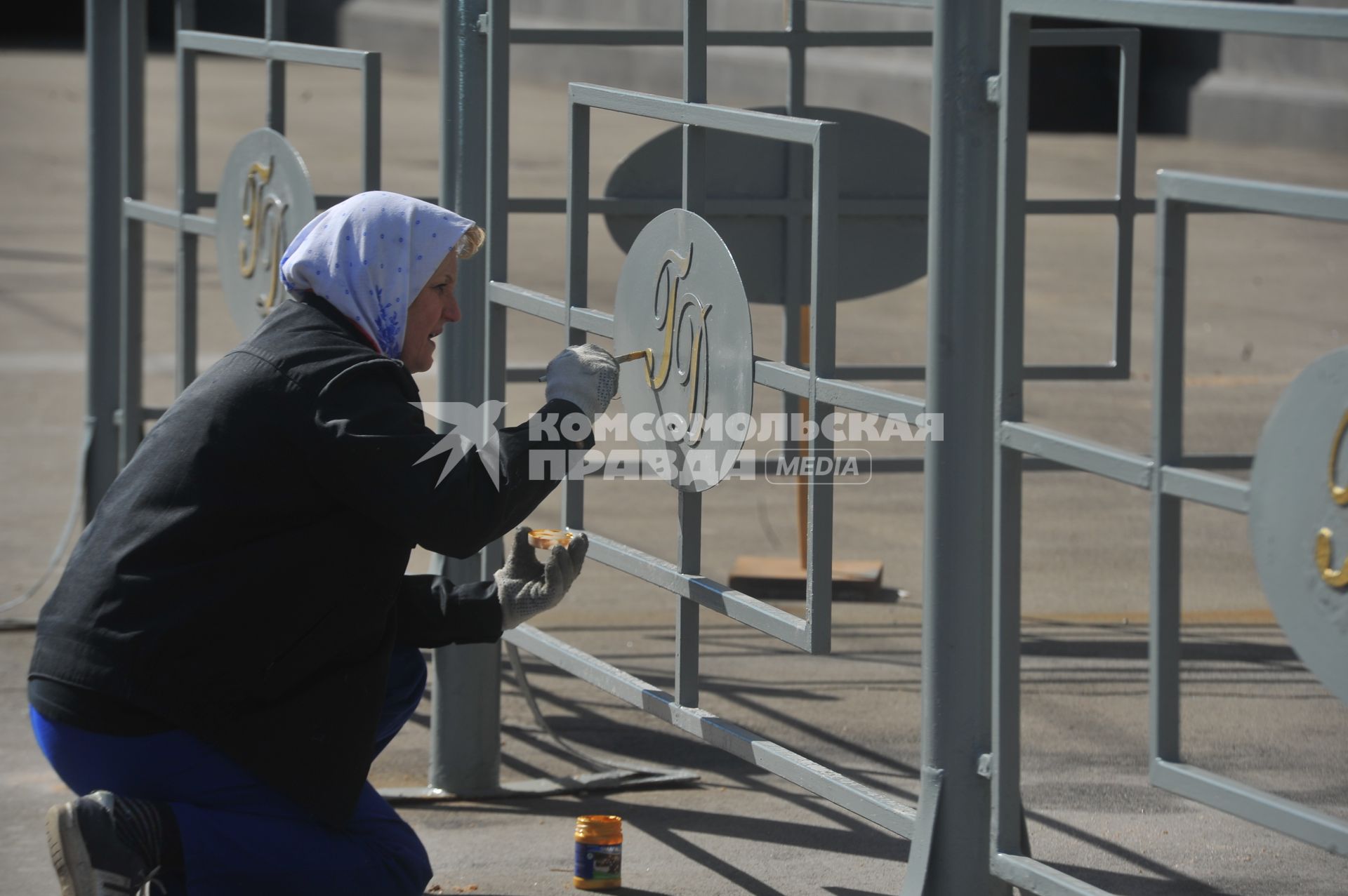 Женщина красит эмблему госдумы перед входом в здание.