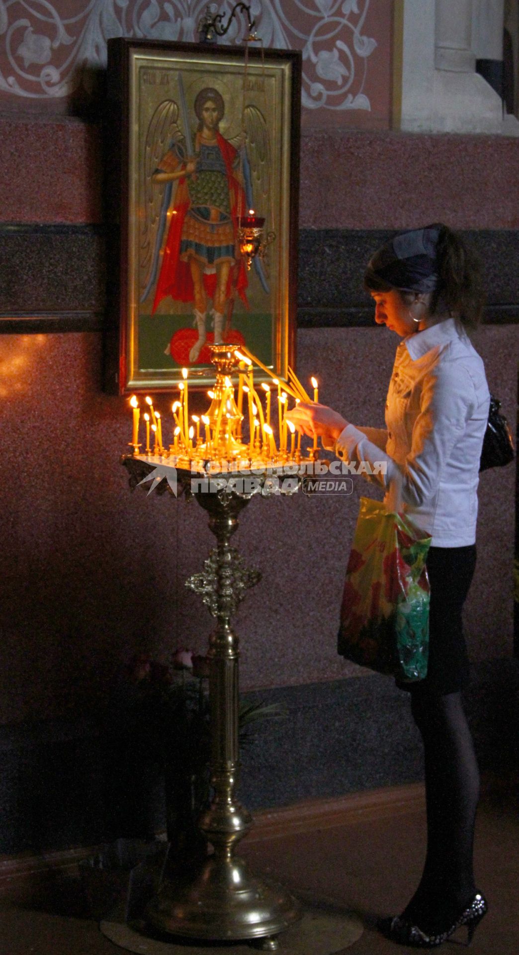 Девушка в церкви ставит свечку в подсвечник.