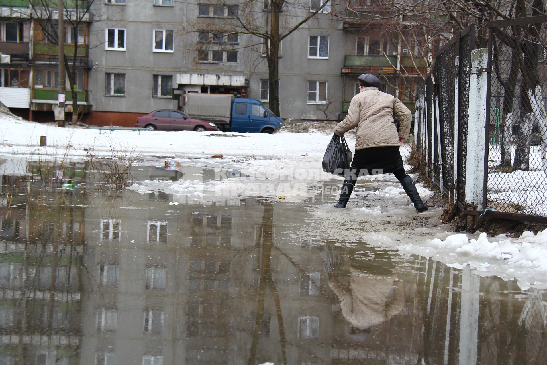 Весенний паводок в городе. Женщина пытается обойти разлив, карабкается по забору.