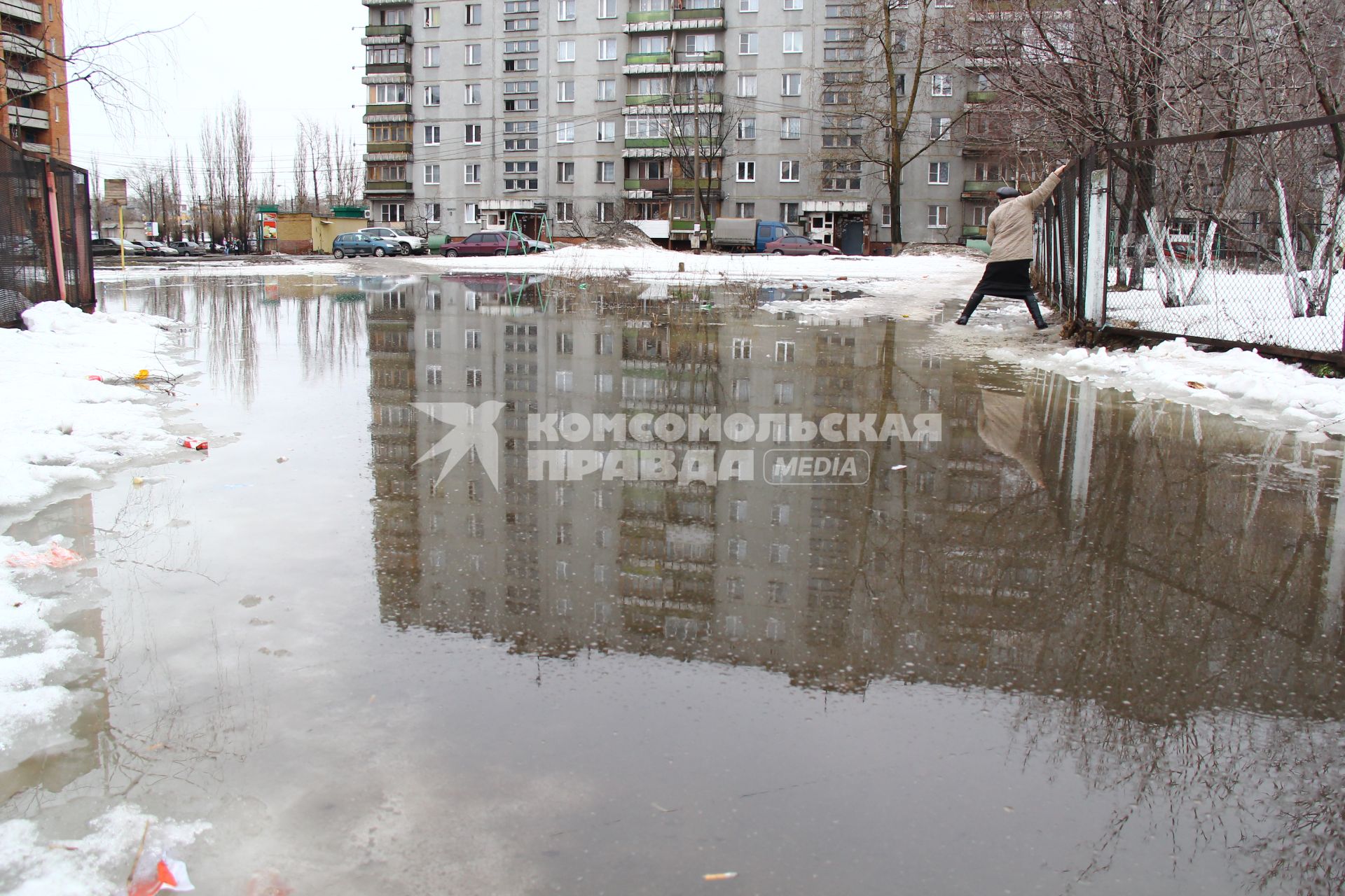 Весенний паводок в городе. Женщина пытается обойти разлив, карабкается по забору.