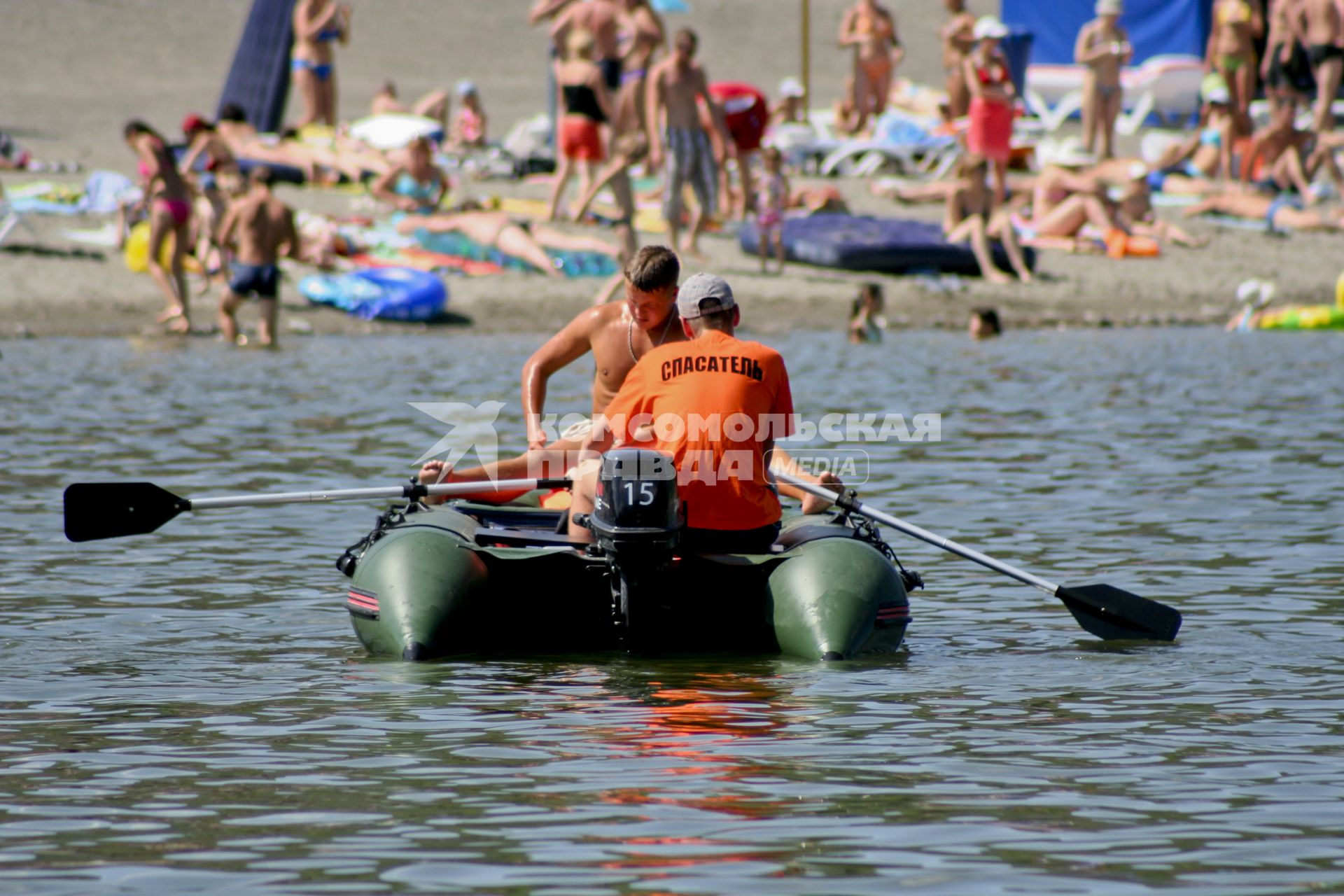 Спасательная моторная лодка  с подвесным лодочным мотором на веслах проходит мимо берега на котором отдыхают туристы.