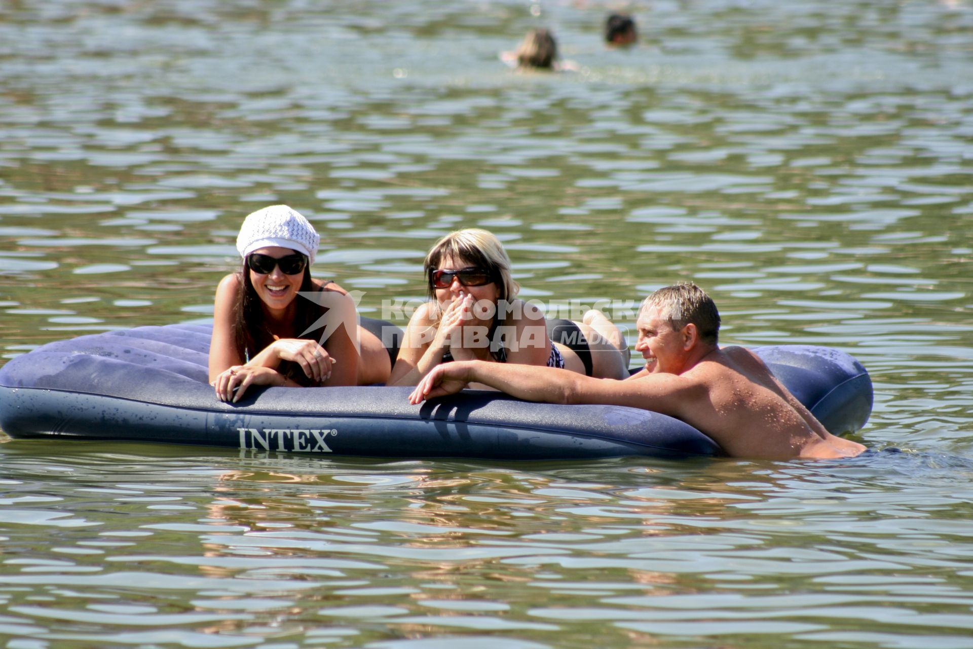 Две девушки лежат на водном матраце `INTEX`, к ним подплыл мужчина.