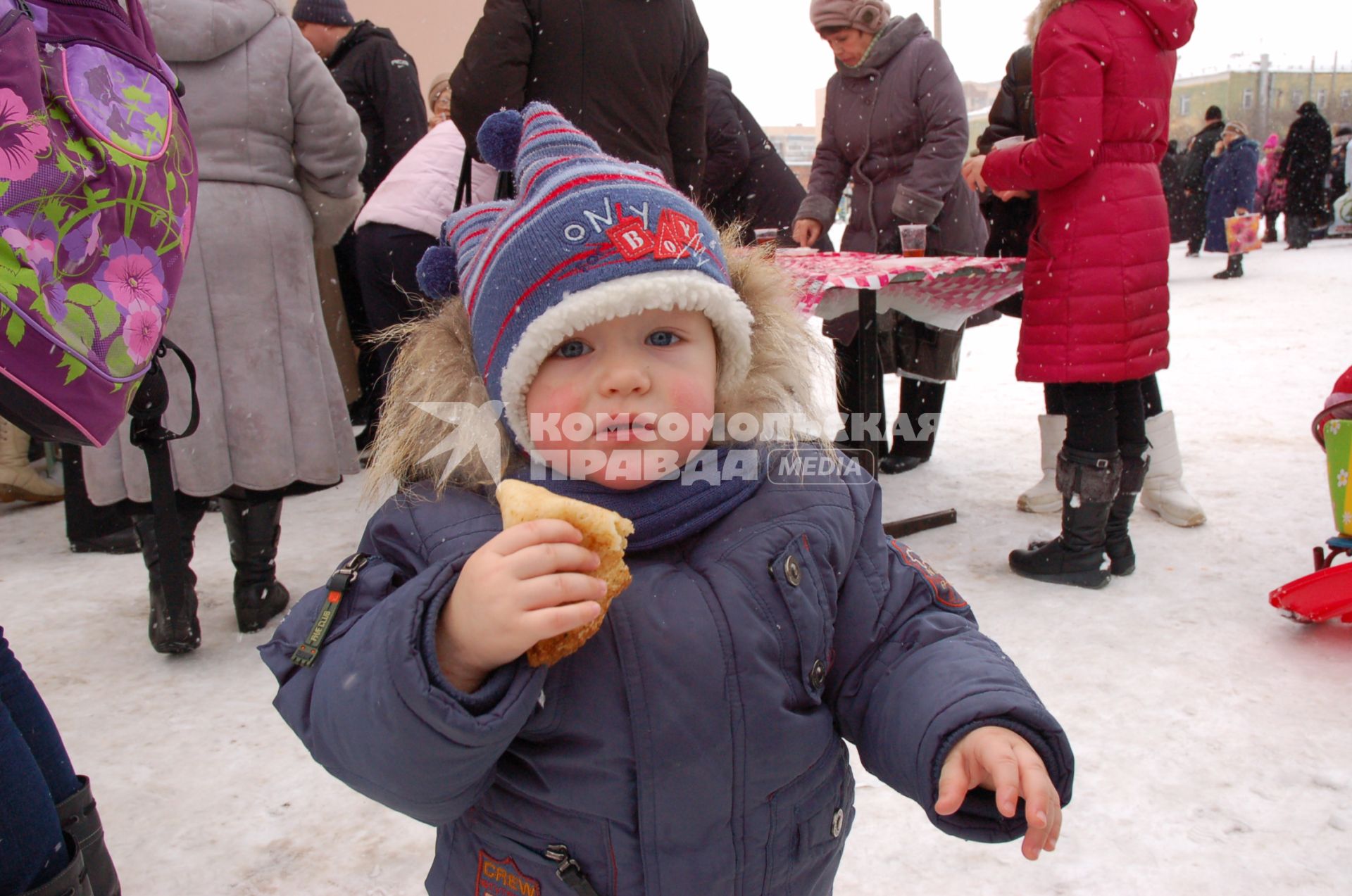 Ребенок с блином в руках на улице.