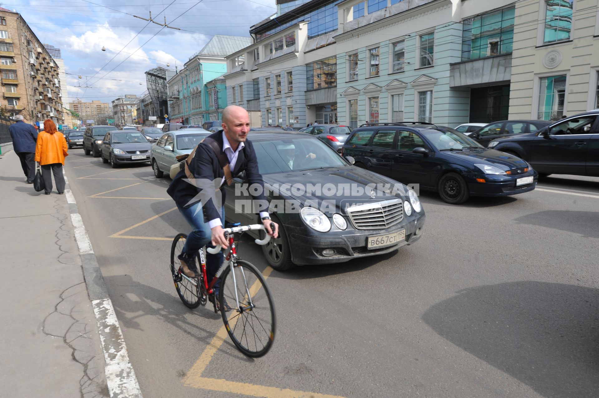 Мужчина едет на велосипеде по обочине автомобильной дороги.