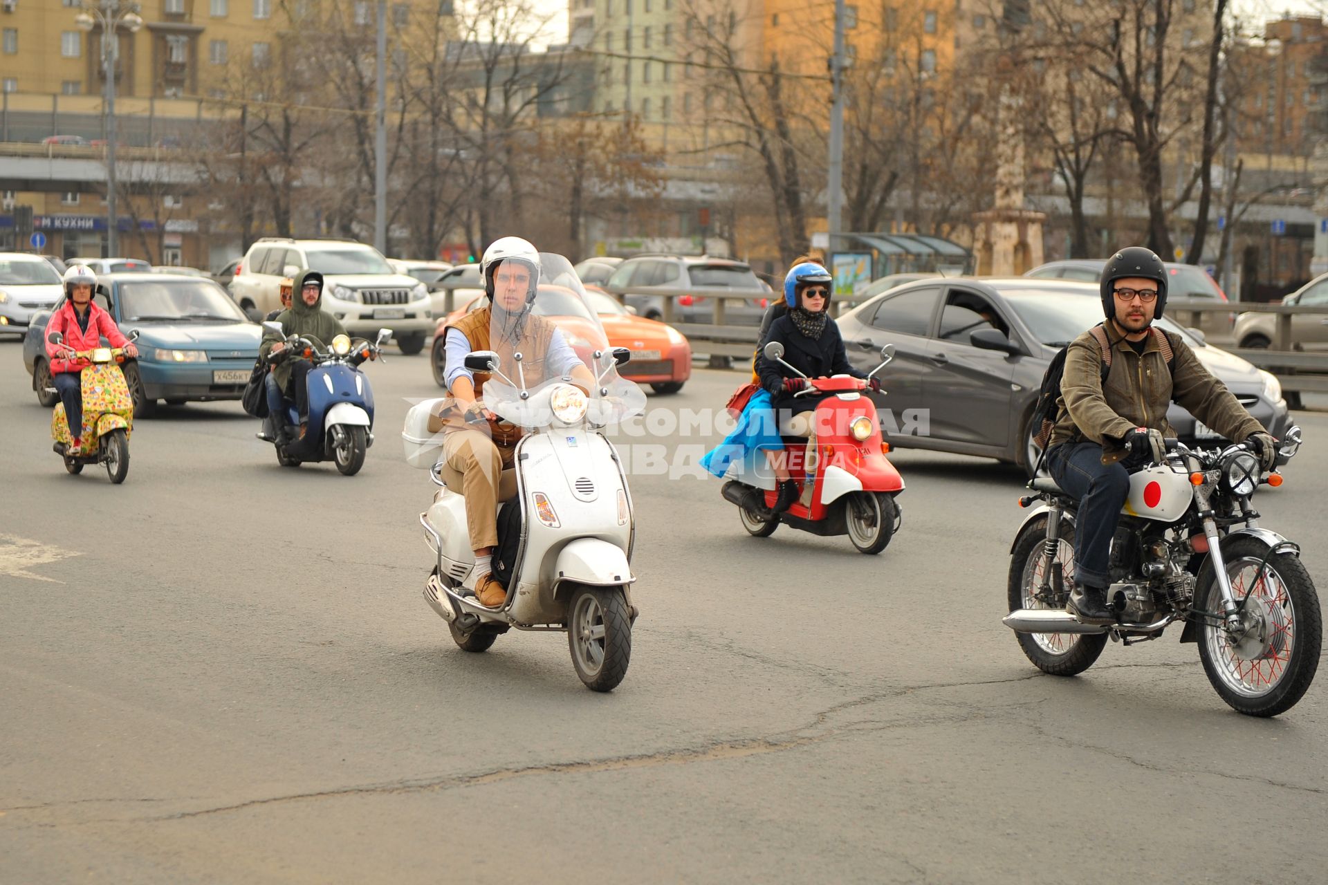 Молодежь едет на скутерах и мопедах по городу.