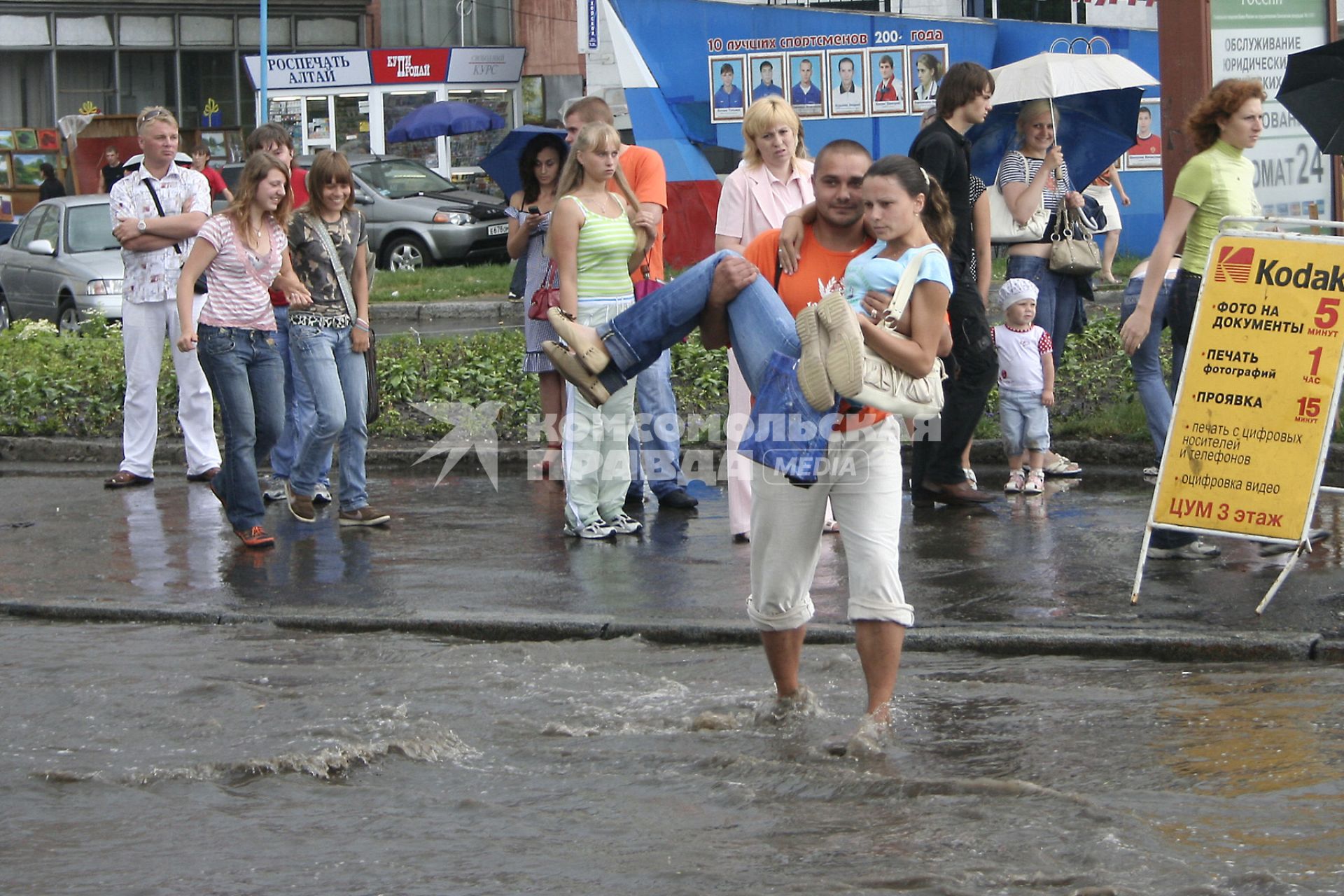 Мужчина переносит девушку через дорогу залитую водой после проливного дождя.