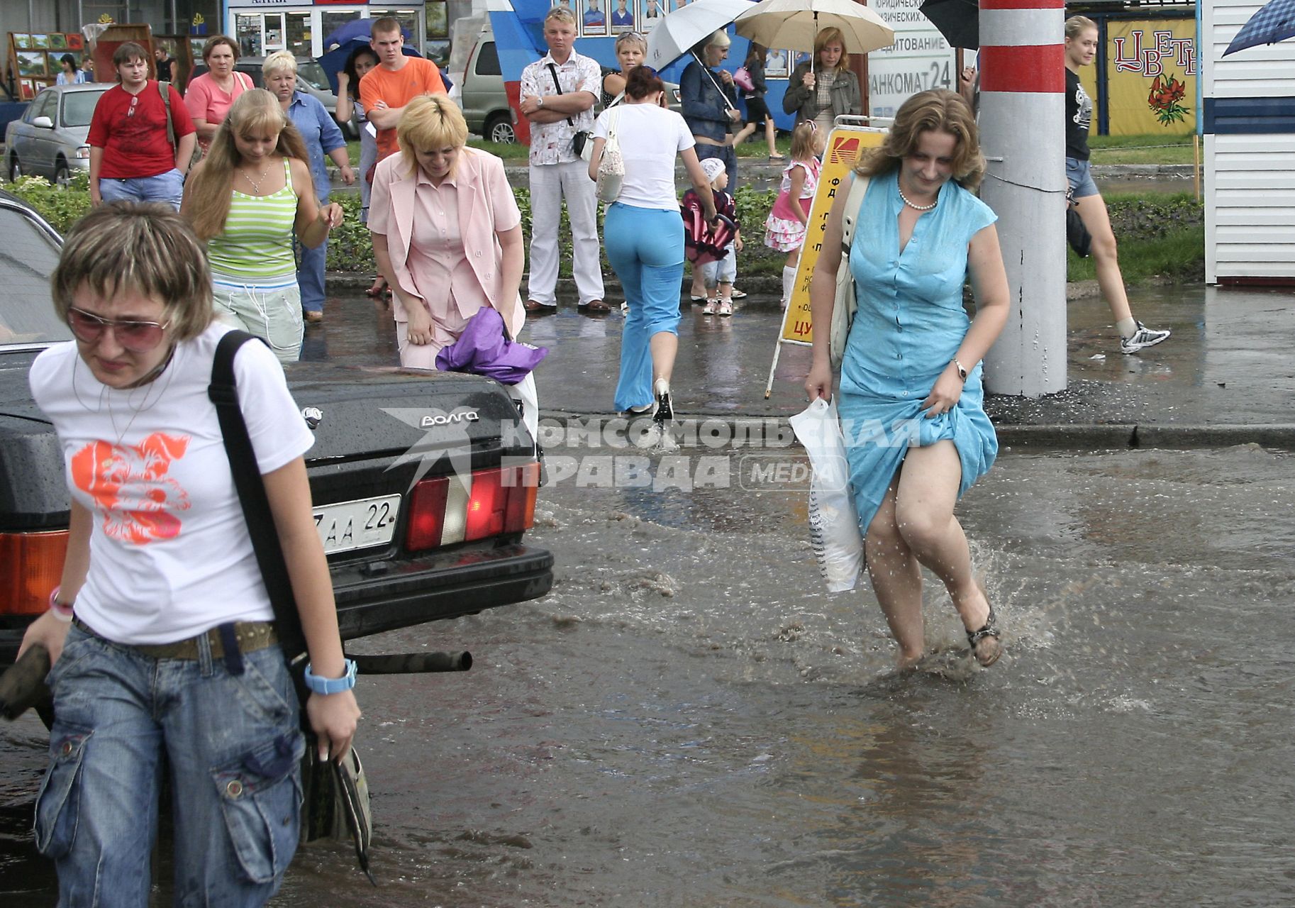 Пешеходы переходят дорогу залитую водой после проливного дождя.