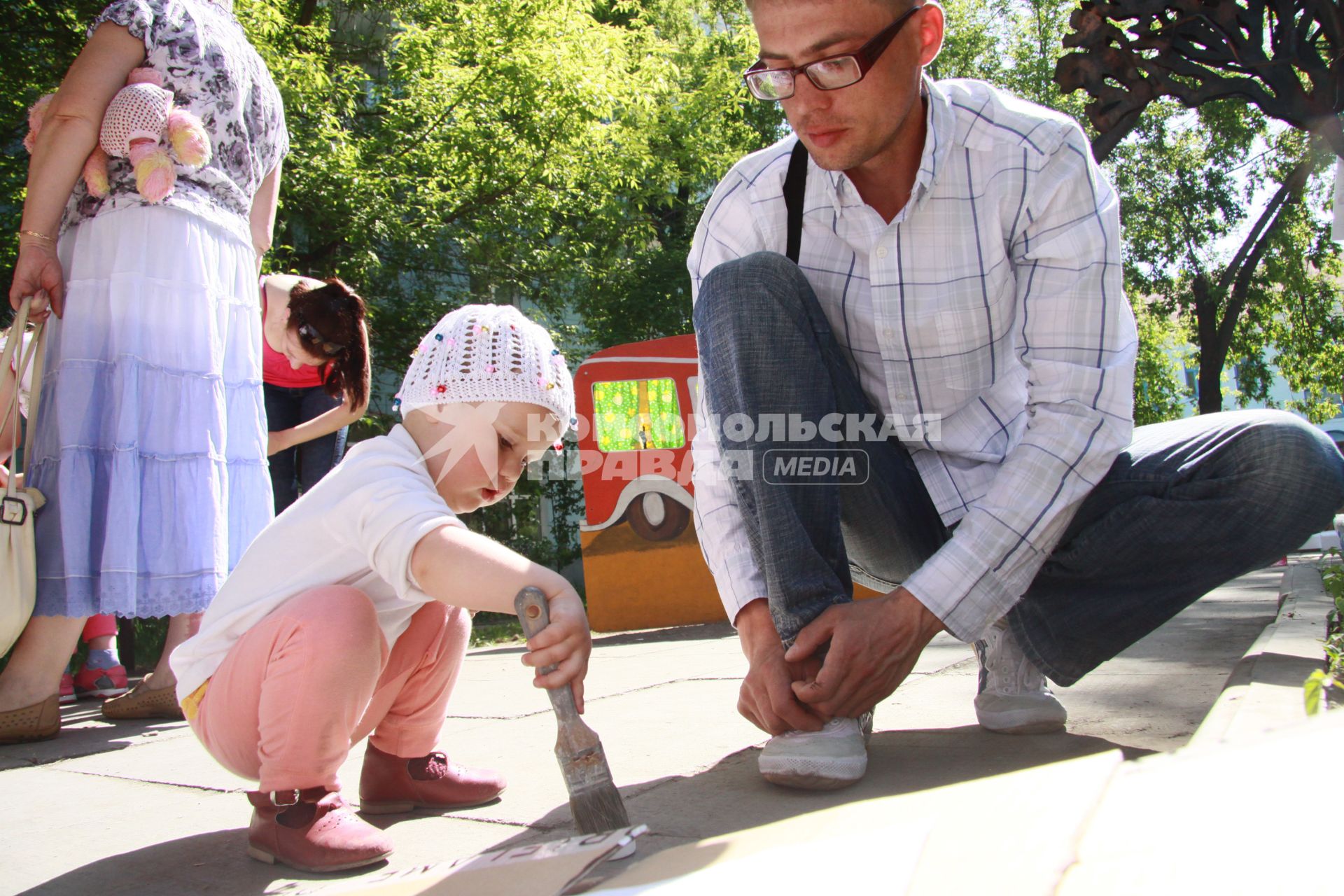 Ребенок с кистью в руках разукрашивает картон под чутким присмотром отца.