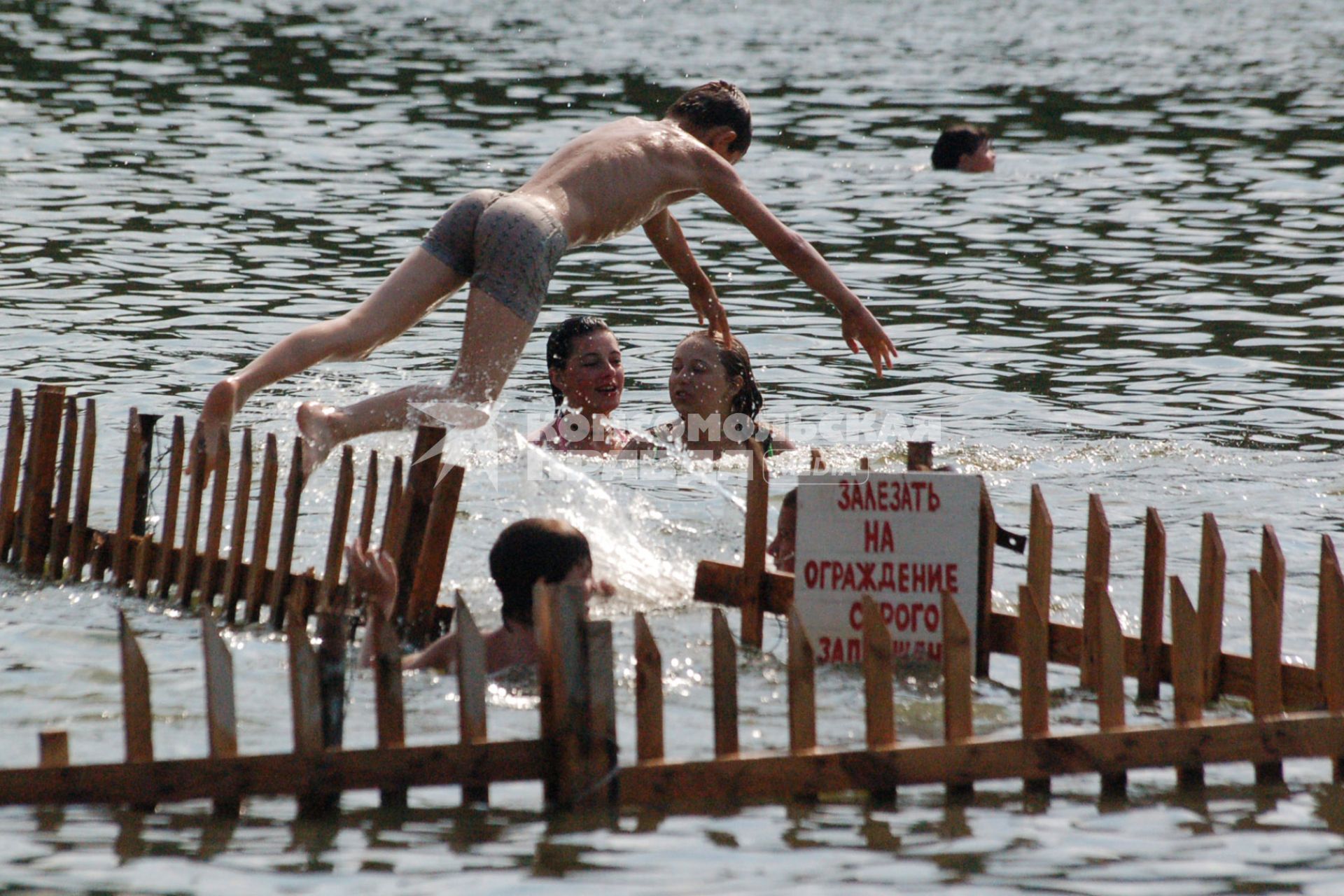 Мальчик прыгает в воду с ограждения на котором прикреплена надпись: `Залезать на ограждение строго запрещено`.