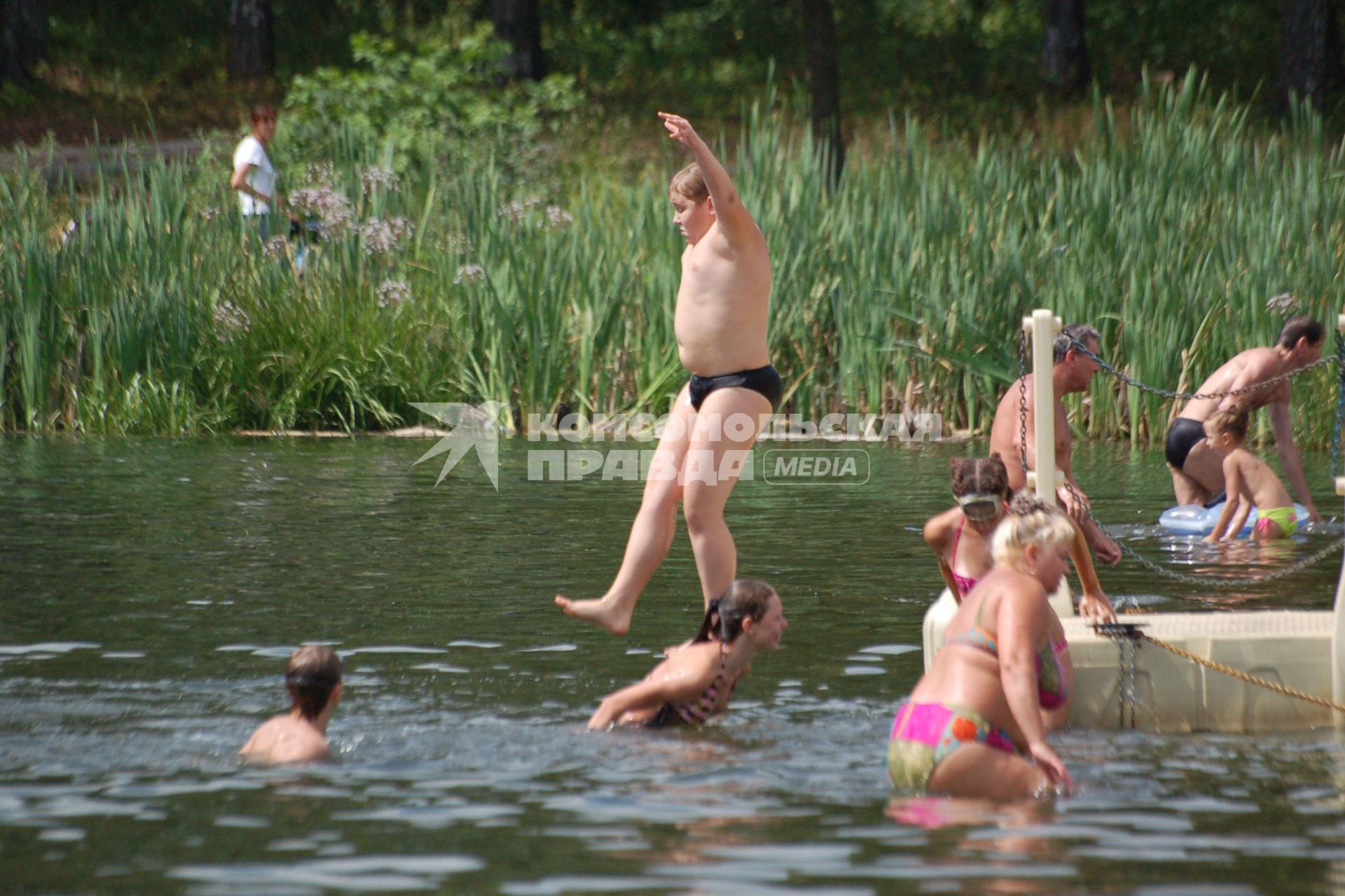 Тучный мальчик прыгает с берега в воду.