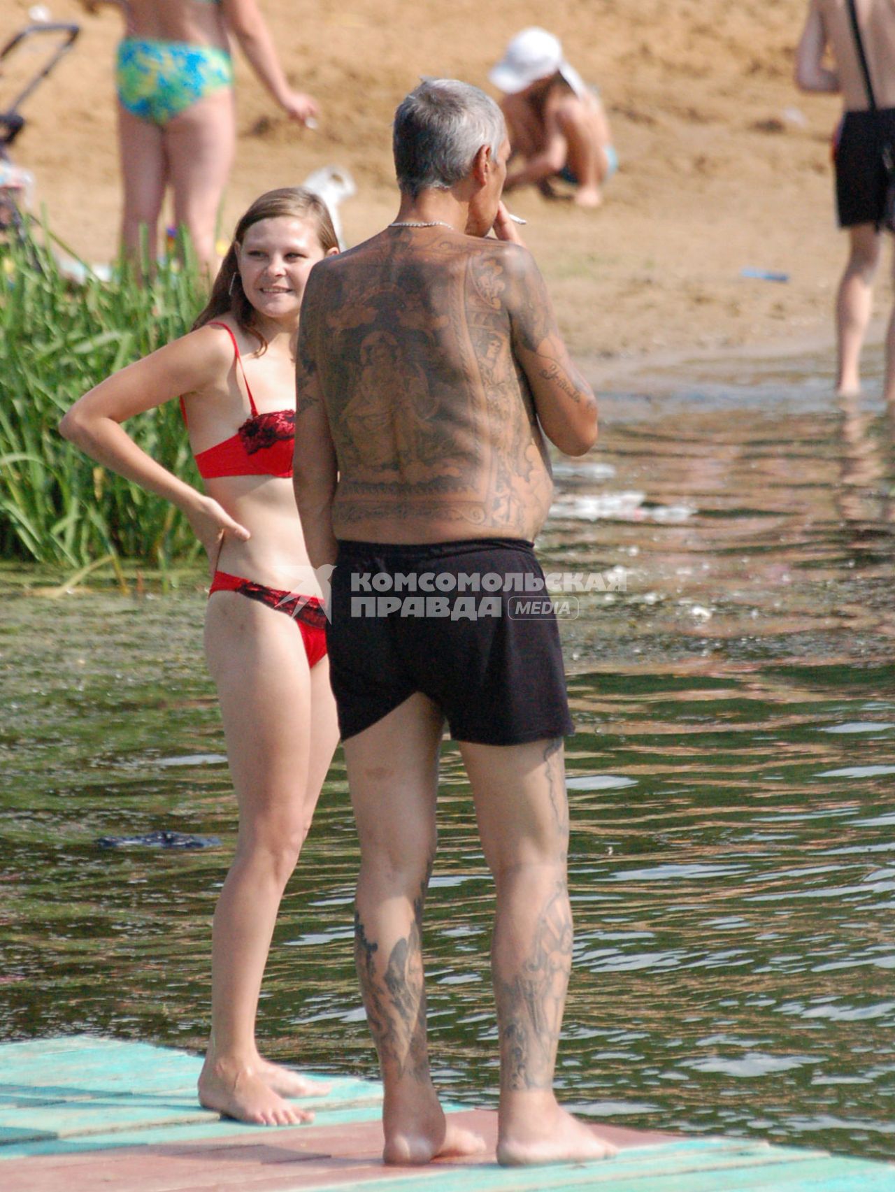 На берегу водоема стоит мужчина весь в наколках (татуировках), рядом с ним стоит девочка.