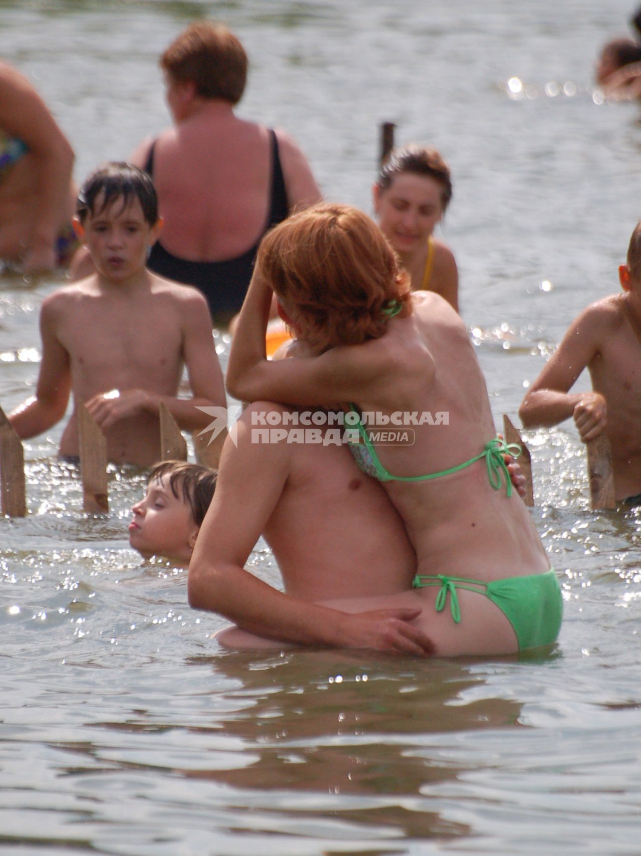 Молодая пара обнявшись стоит в воде.